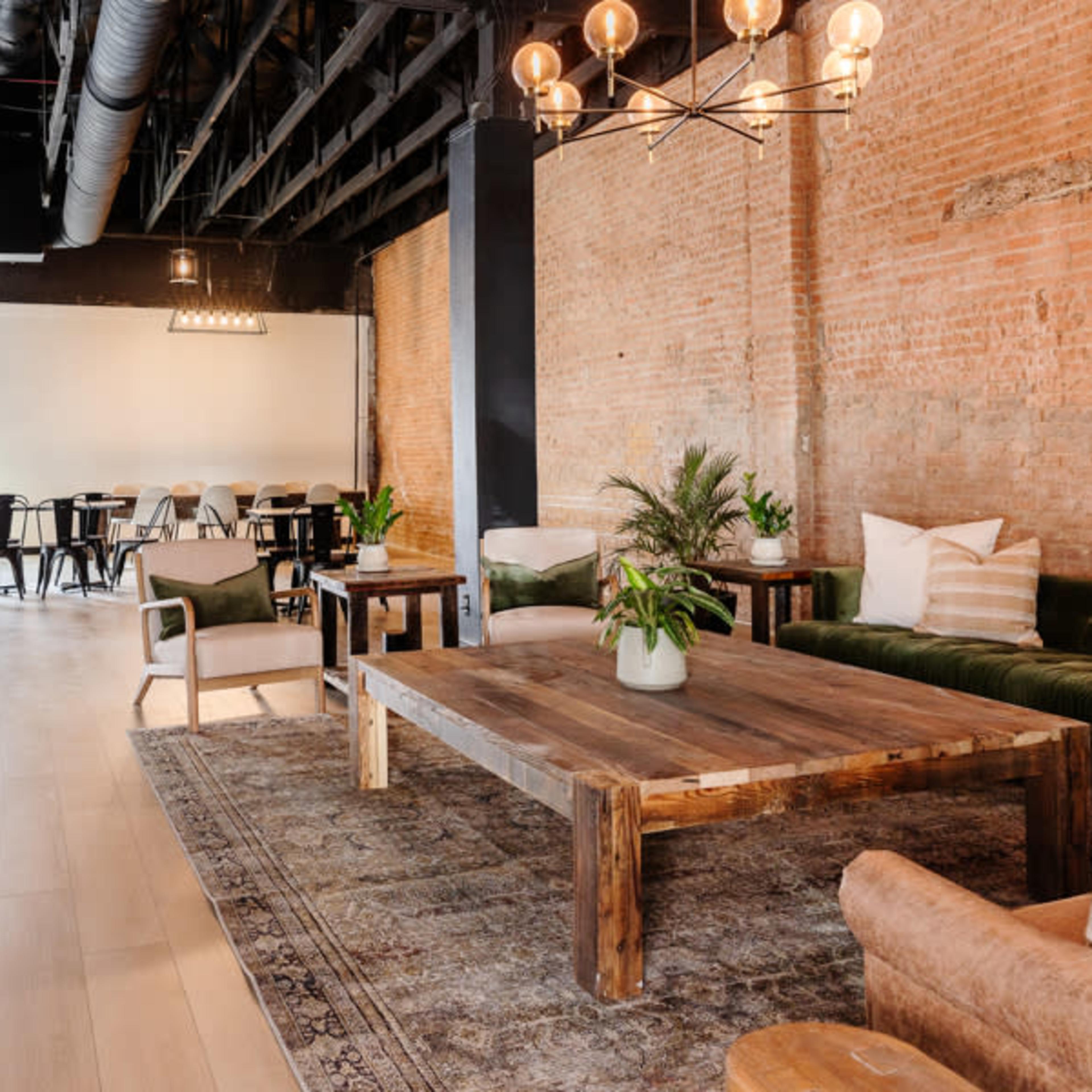 A spacious lounge area with exposed brick walls, a large wooden coffee table, and a mix of seating options, including couches and chairs.