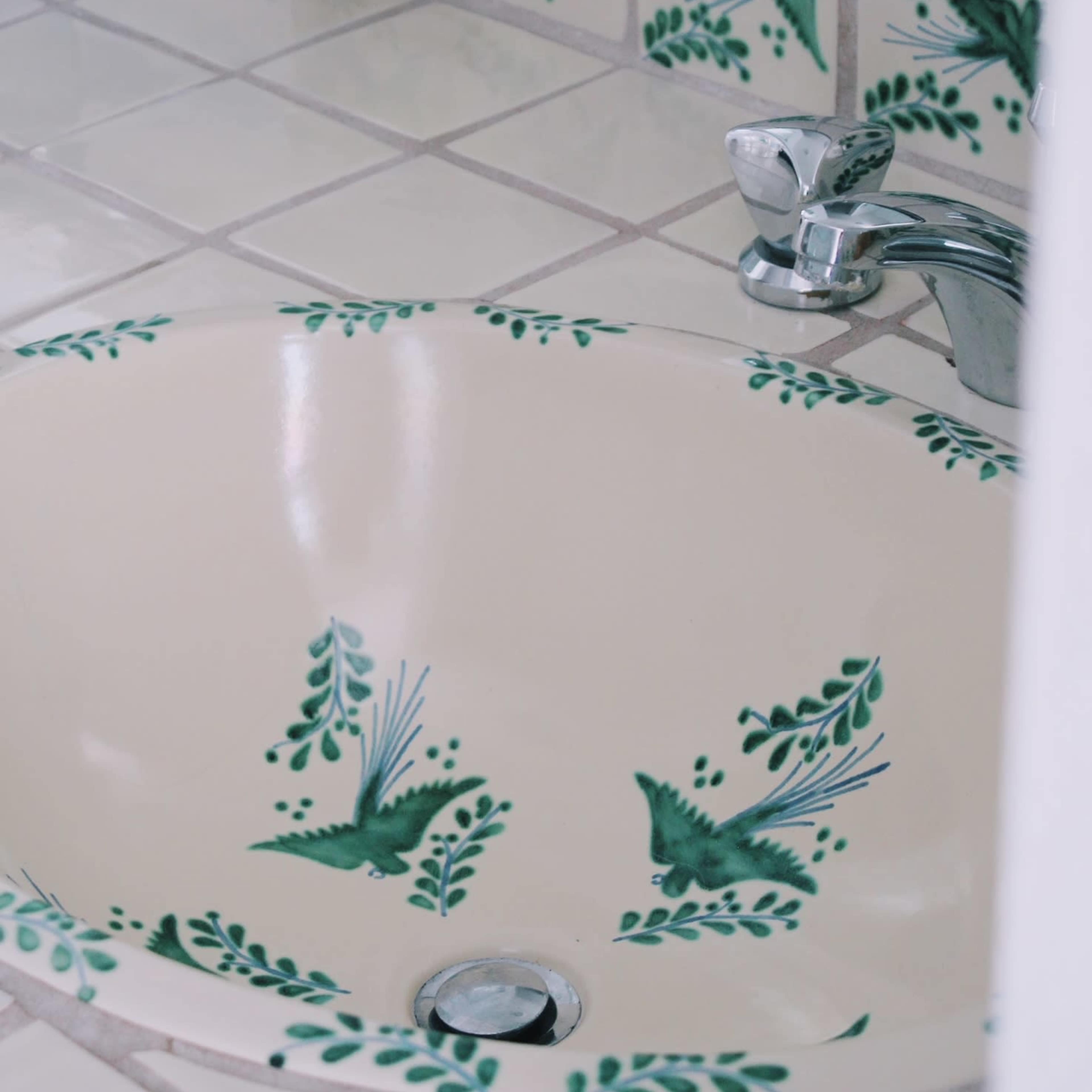 A round sink with decorative green bird and leaf patterns around the edge, set in a tiled countertop.