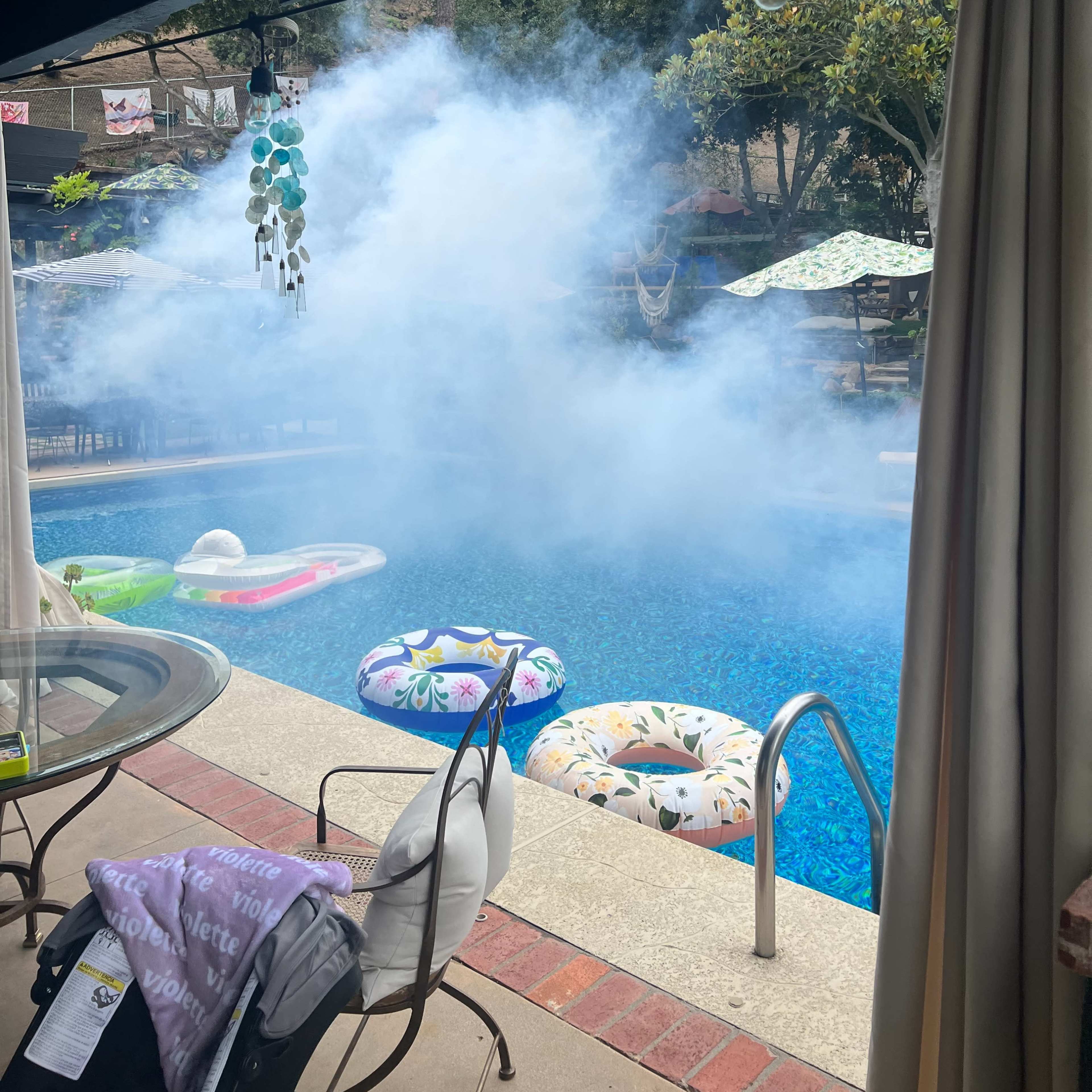 A pool surrounded by colorful floats is partially obscured by a cloud of mist.