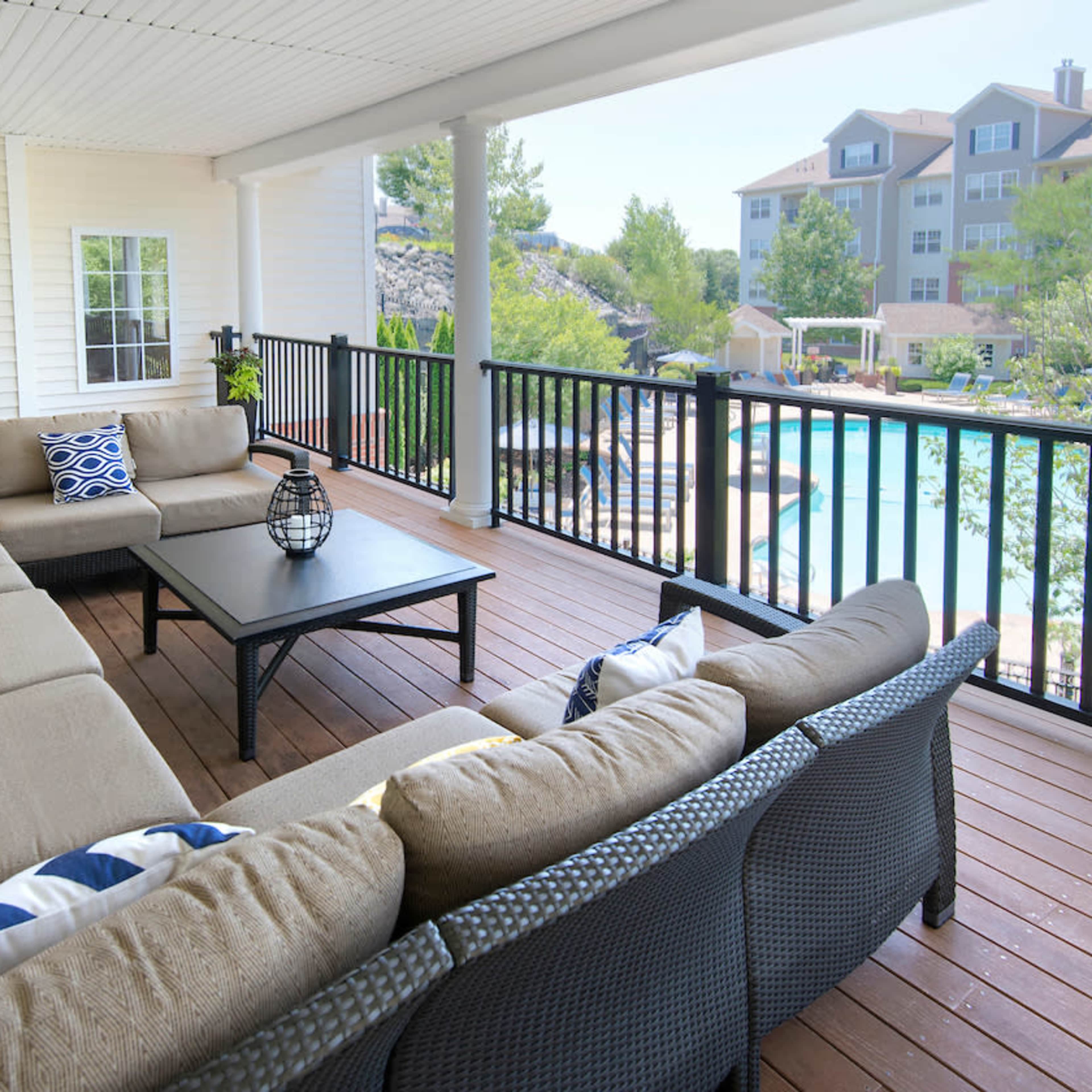 A spacious outdoor lounge area features a large sectional sofa arranged around a central table, overlooking a swimming pool and resort-style buildings.