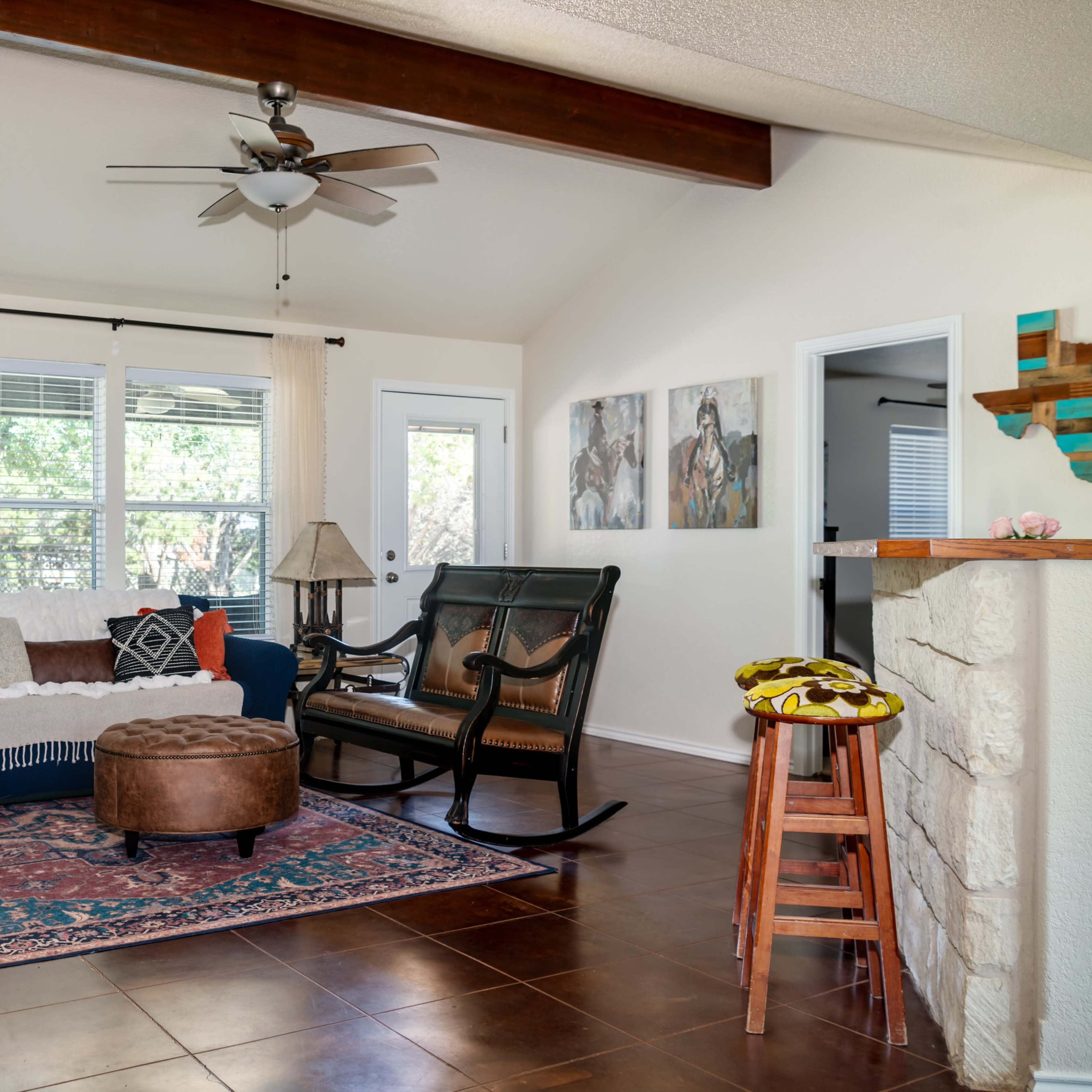The living room features a blue couch, a brown ottoman, a rocking chair, and a small kitchenette with a stone bar.