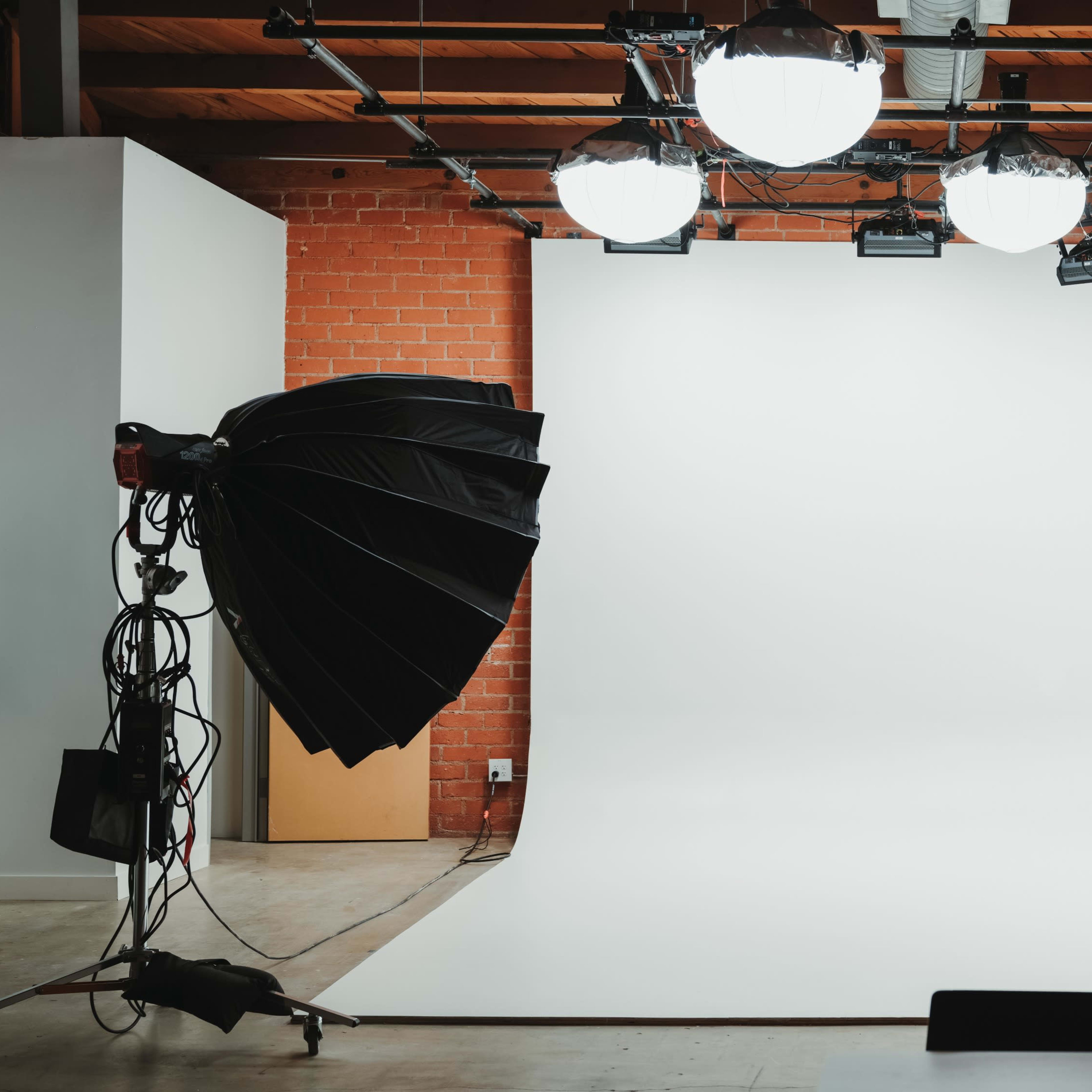 A photography studio features a seamless white backdrop with multiple overhead lights and a large softbox positioned to the side.