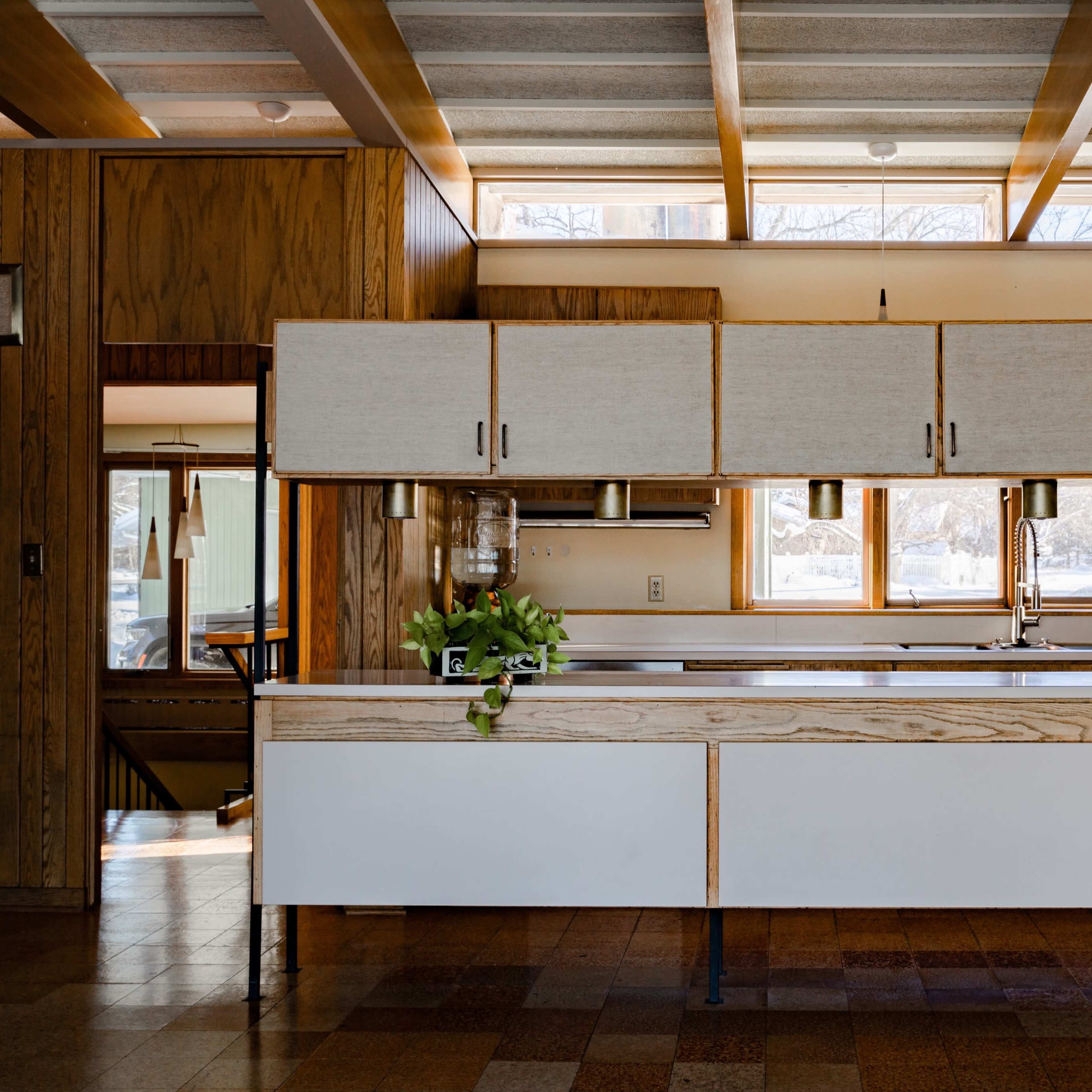 A modern kitchen features a central island with a wooden base, overhead storage cabinets, and large windows allowing natural light to enter.