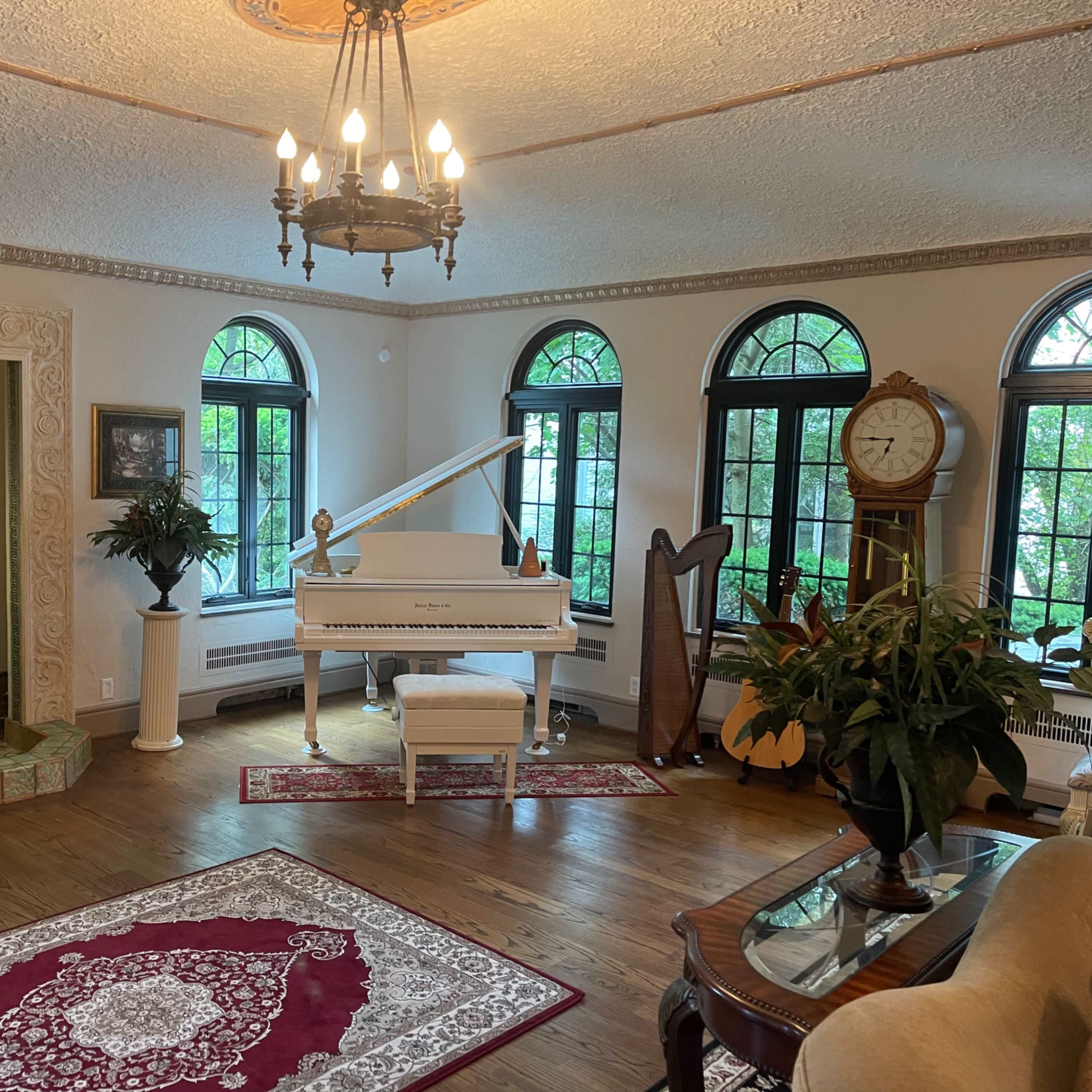 A richly appointed room featuring a grand piano, a harp, large windows, and decorative furnishings in a cozy layout.