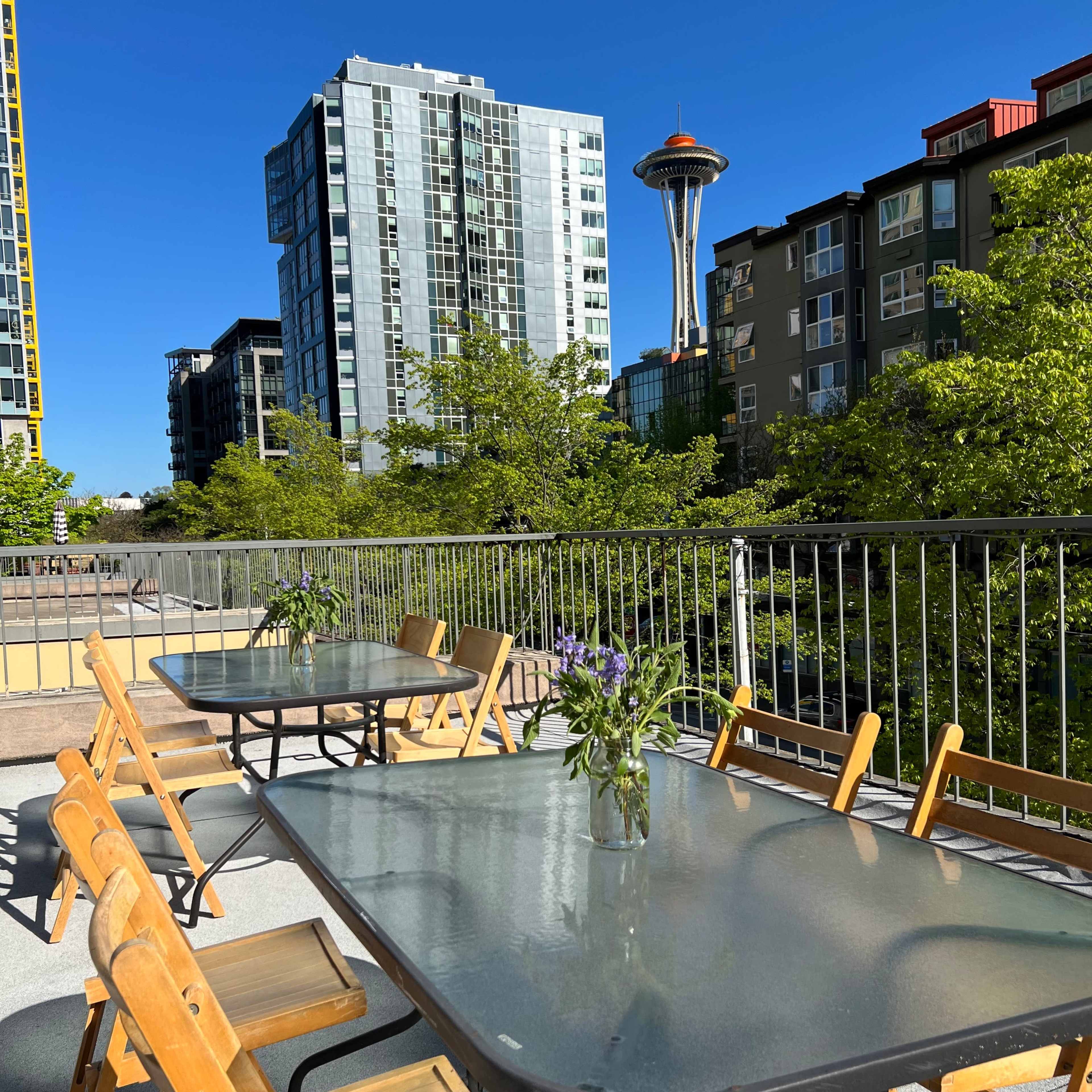 A patio with wooden chairs and tables overlooks the Seattle skyline, featuring the Space Needle in the background.