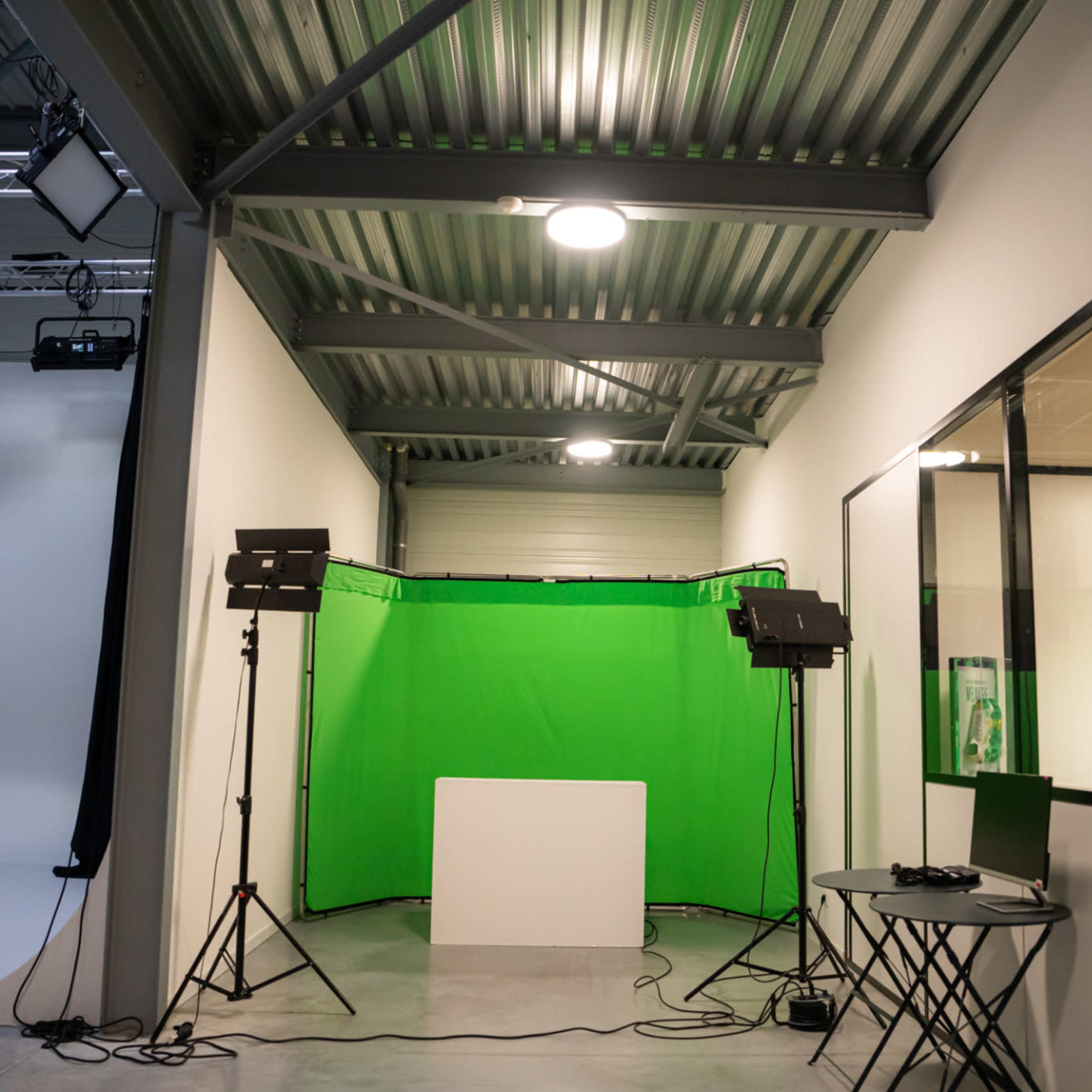 A studio space featuring a green screen backdrop, lighting equipment, and a small table with chairs.