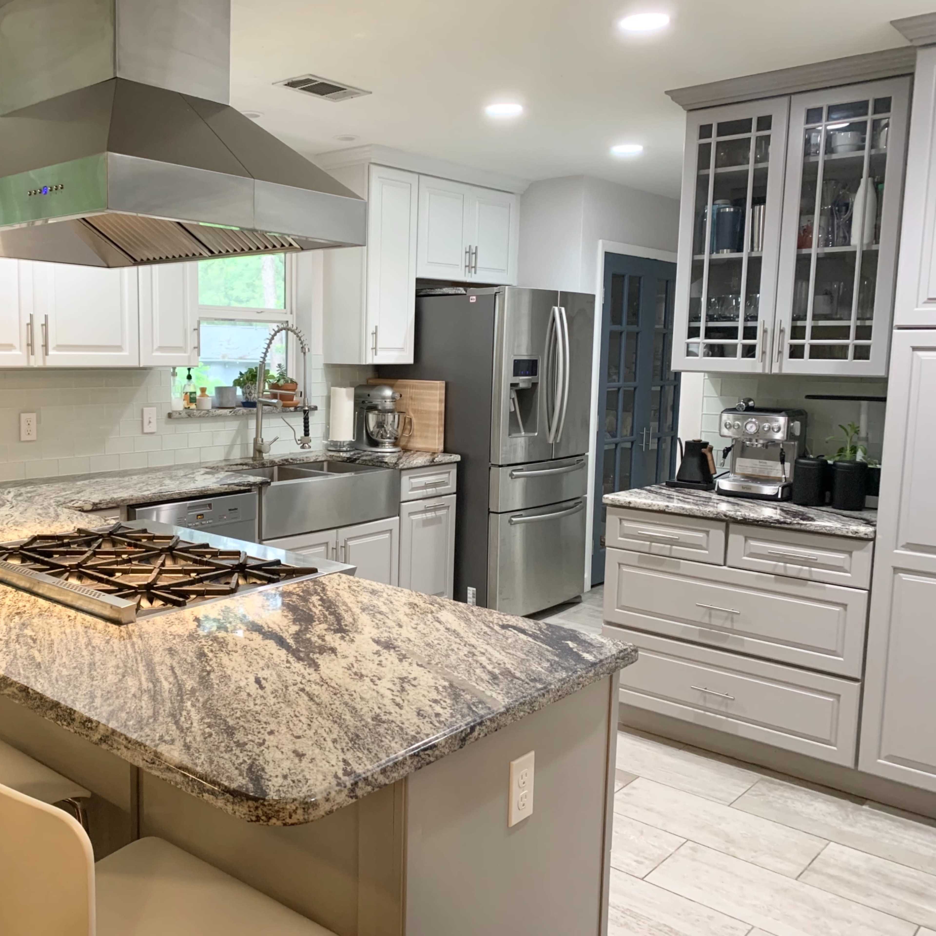 A modern kitchen featuring a large island with a gas stove, stainless steel appliances, and white cabinetry.