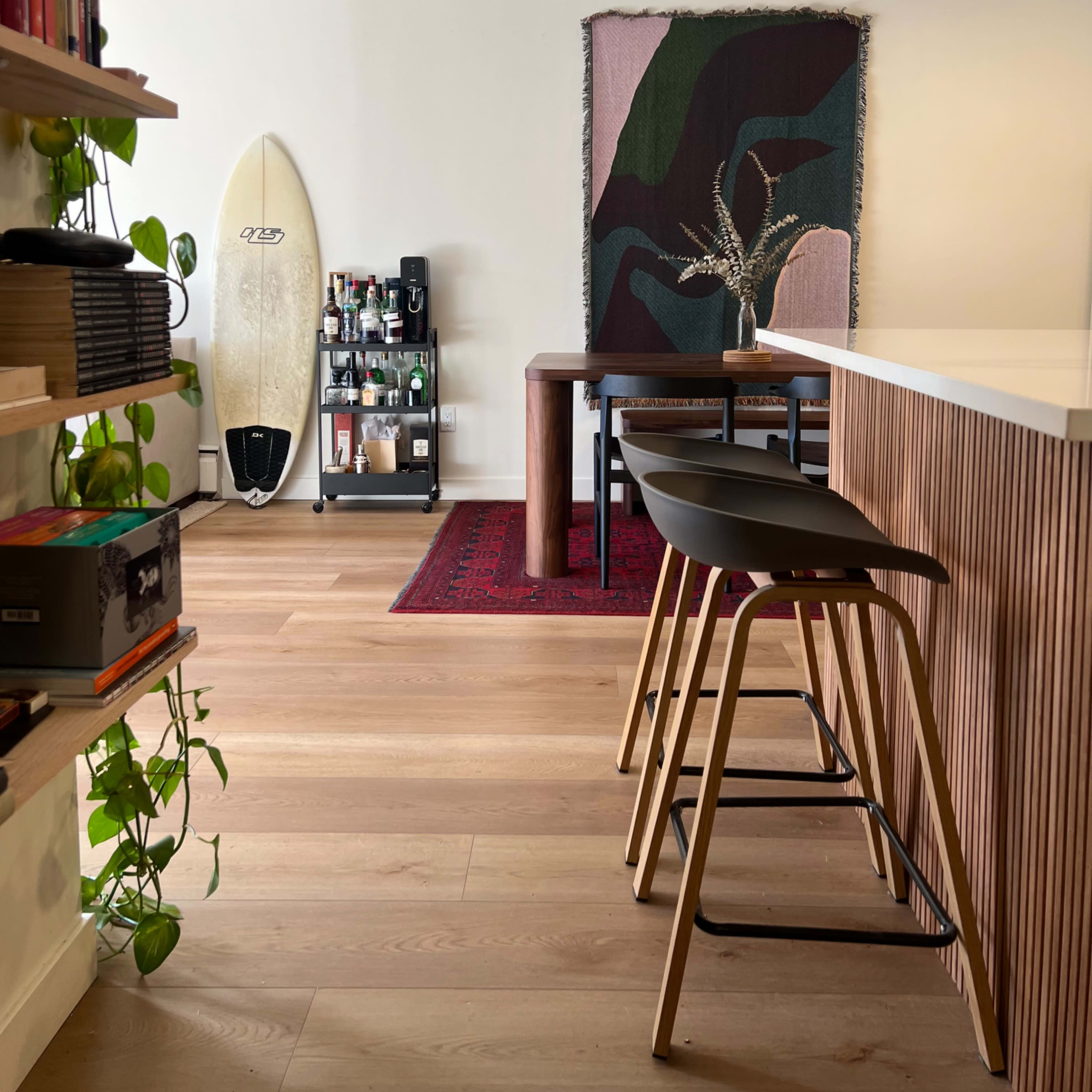 A modern living space featuring a surfboard against a wall, a wooden table with chairs, and a decorative rug.