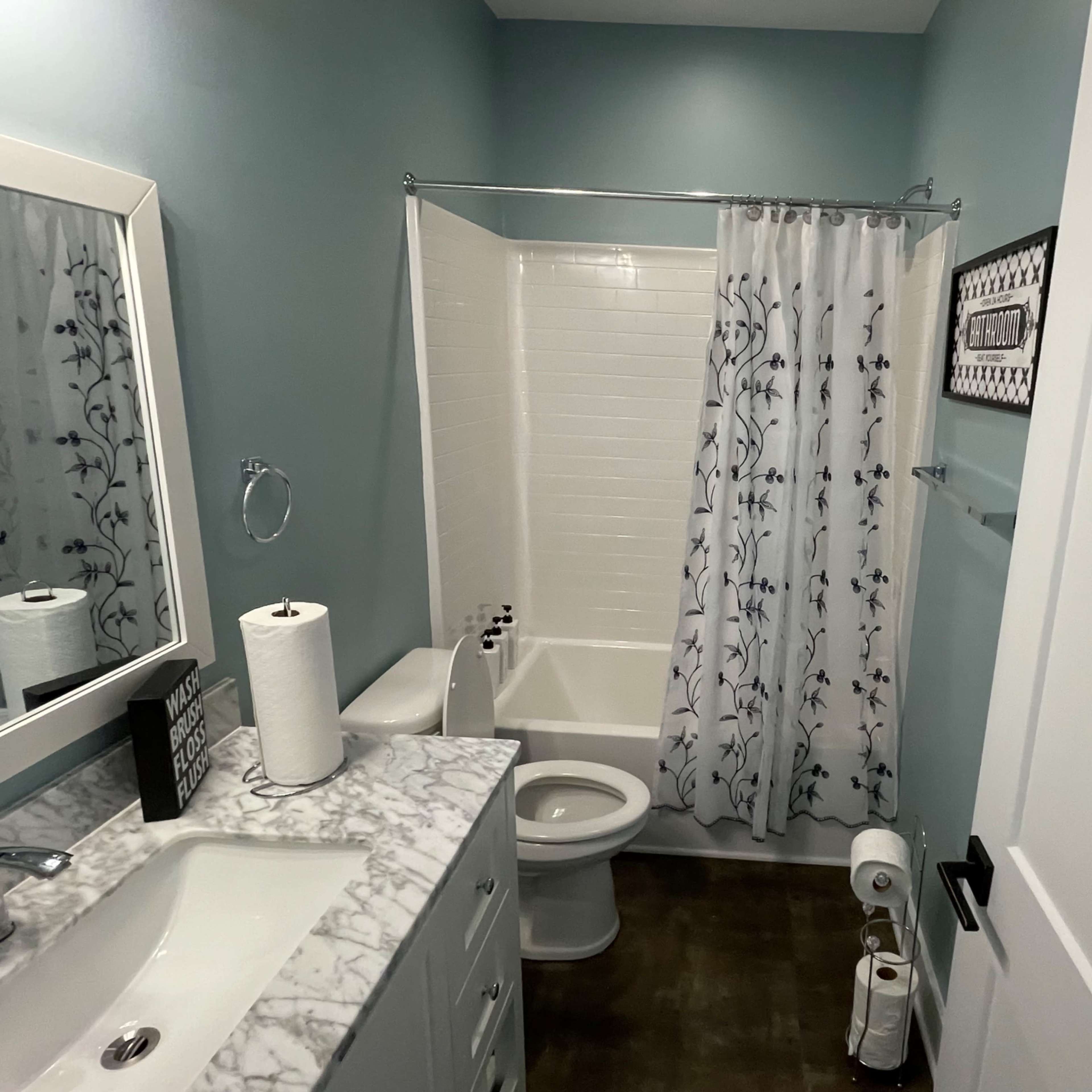 A bathroom with a tub-shower combination, a white marble countertop, and a mirror above the sink.