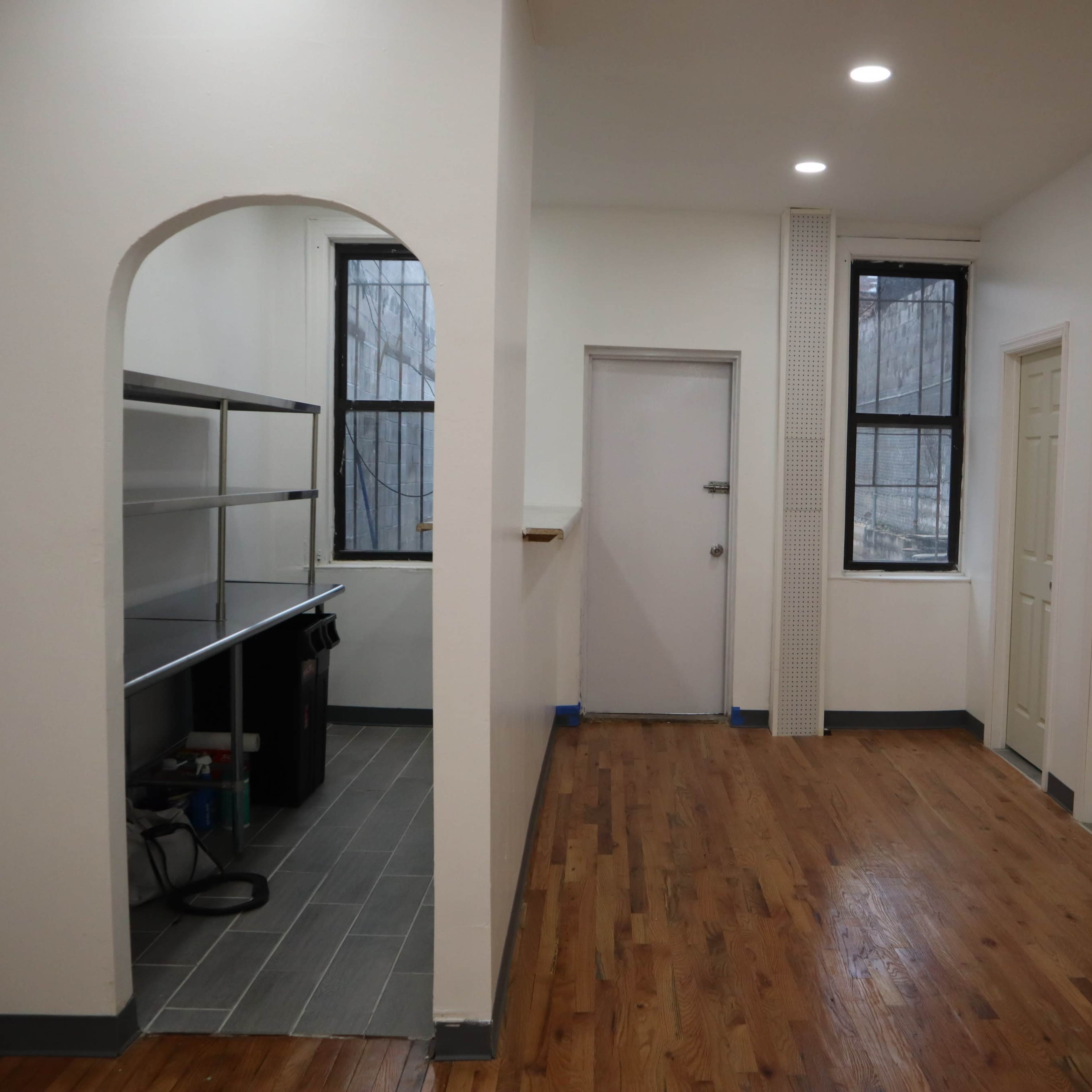 A hallway in an apartment, featuring an archway leading to a kitchen area with shelves, a door at the end, and two closed doors on the right.