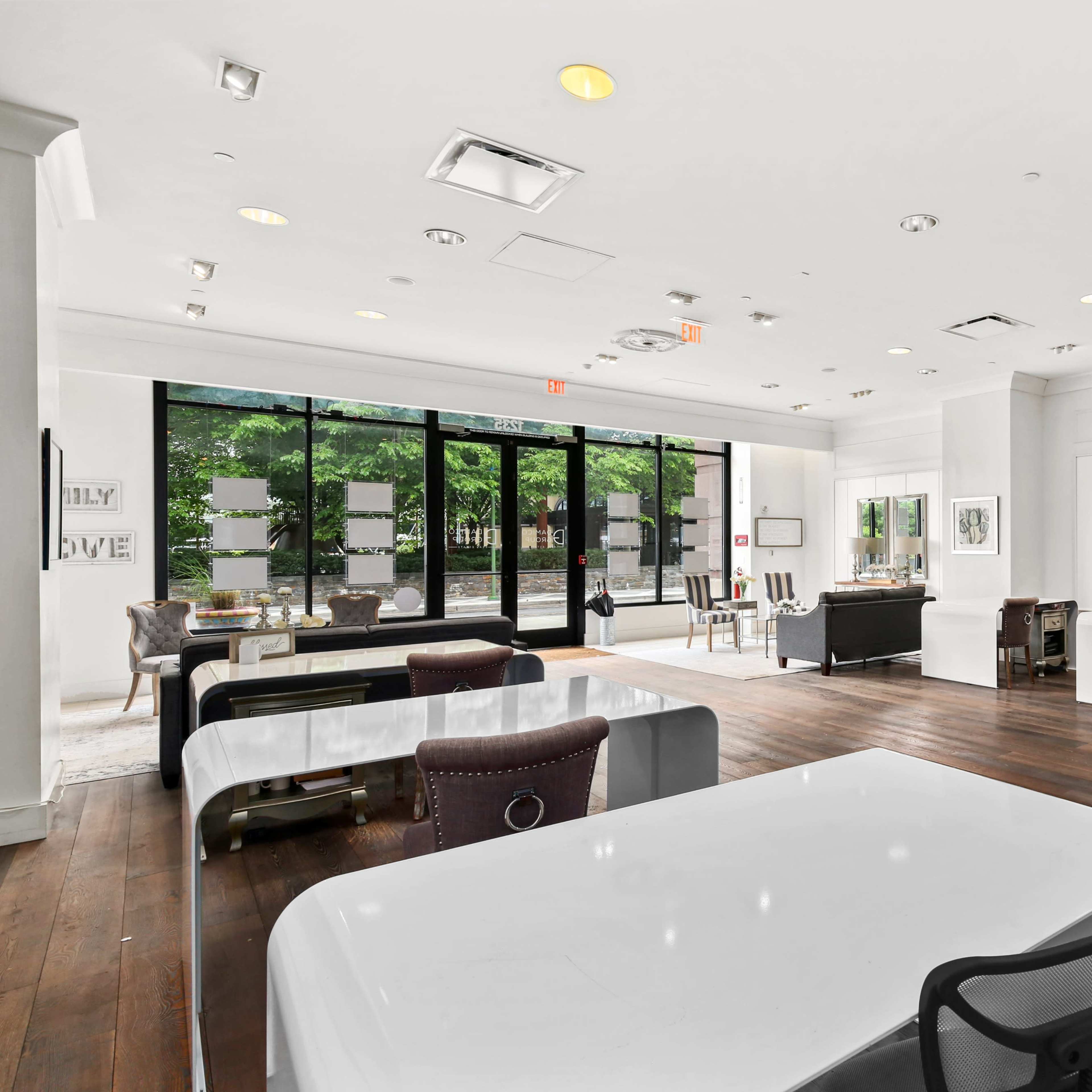 A spacious, modern office interior with large windows, white walls, and wooden floors, featuring desks, chairs, and a ping pong table.