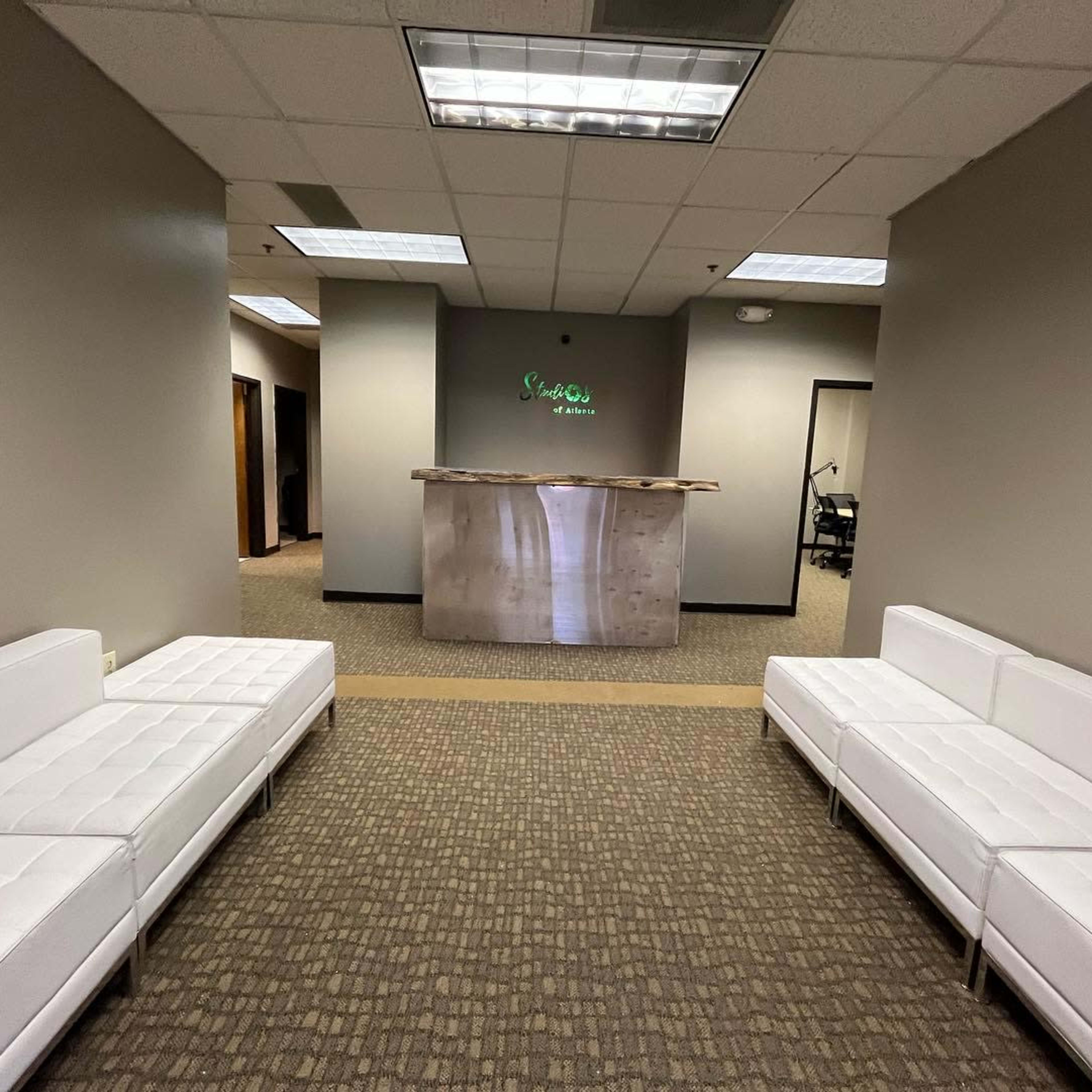A waiting area with two white sofas facing a reception desk in a modern office environment.