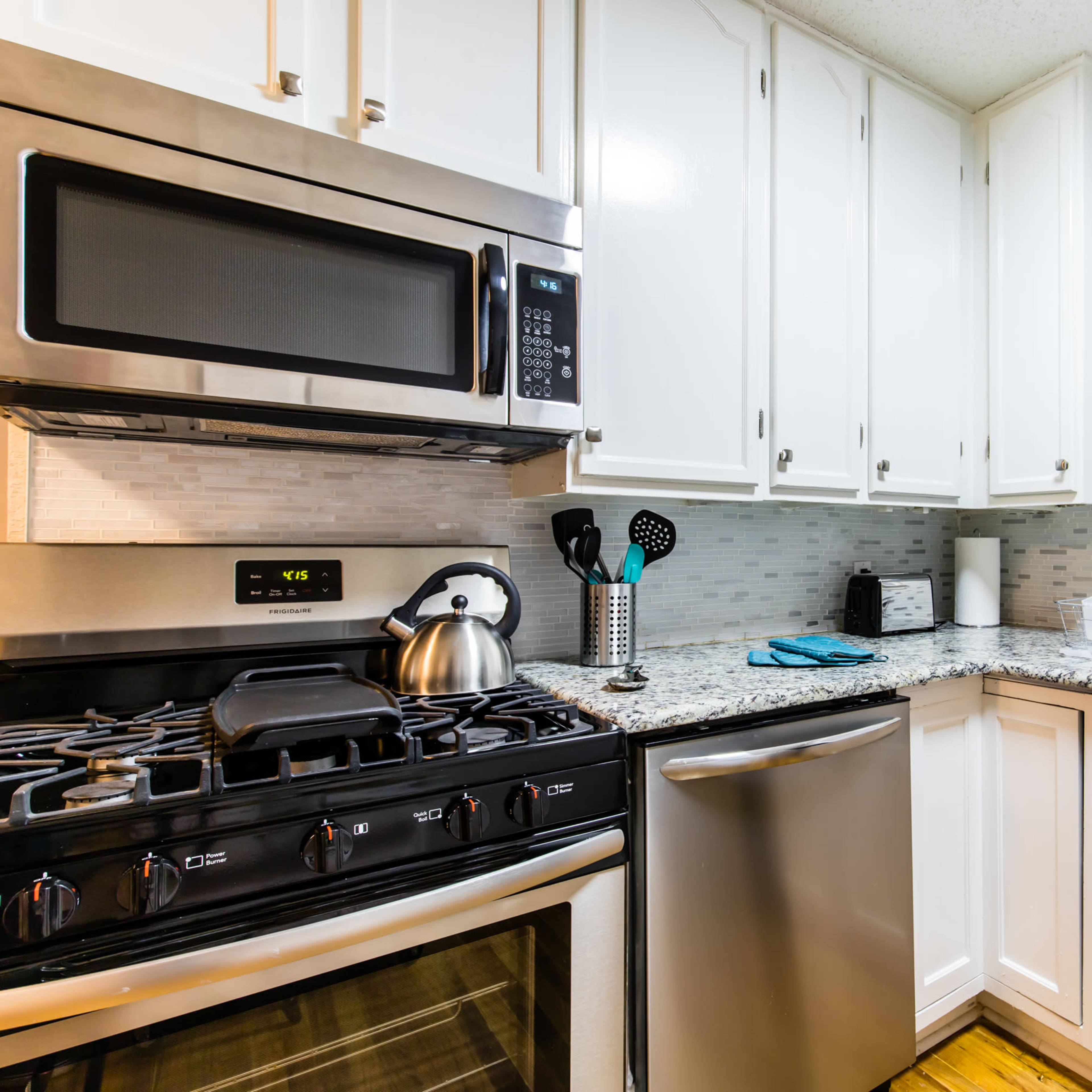 A modern kitchen features stainless steel appliances, white cabinetry, and granite countertops with a sink and window.