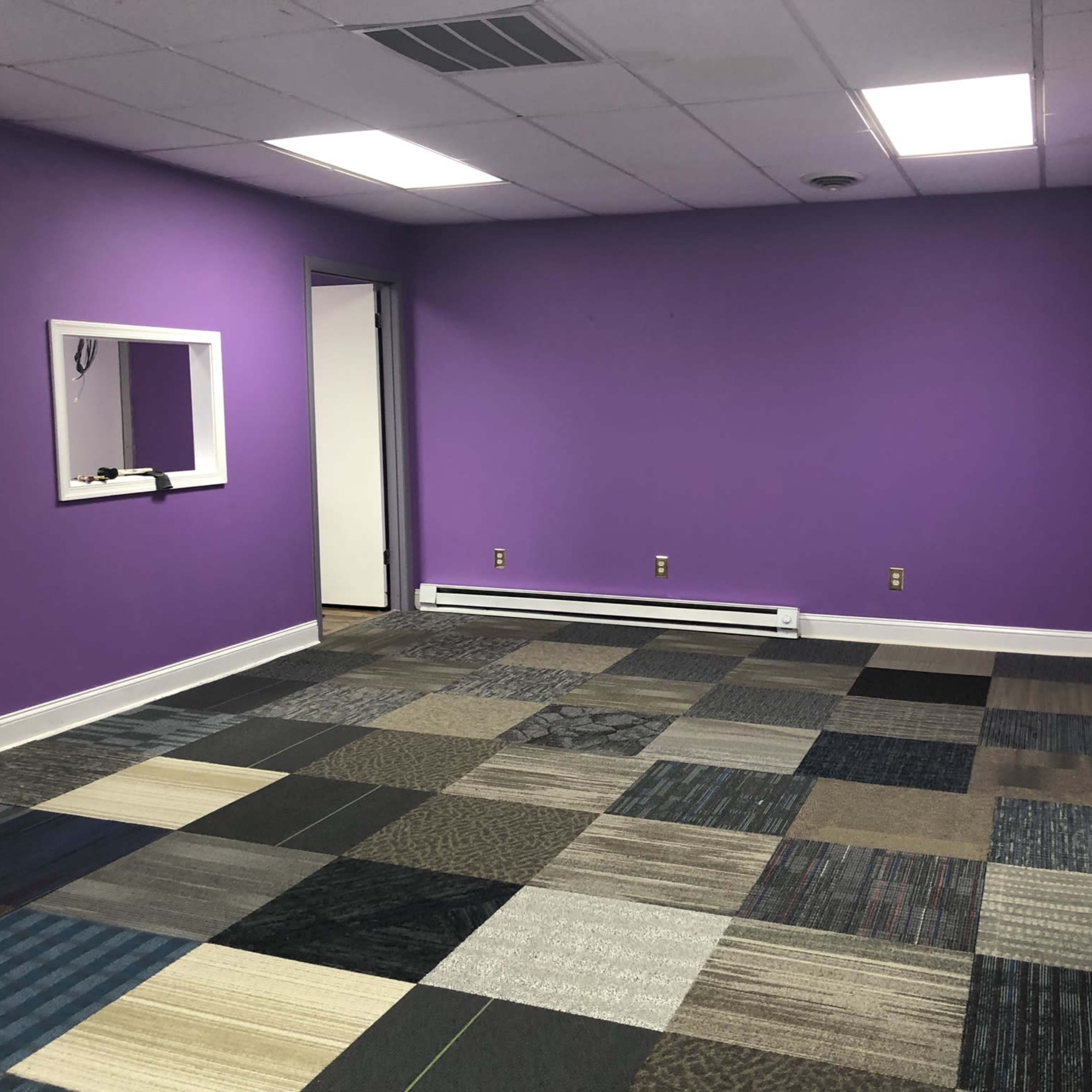 The room features purple walls, a window nook, and a floor covered in various gray and blue carpet tiles.