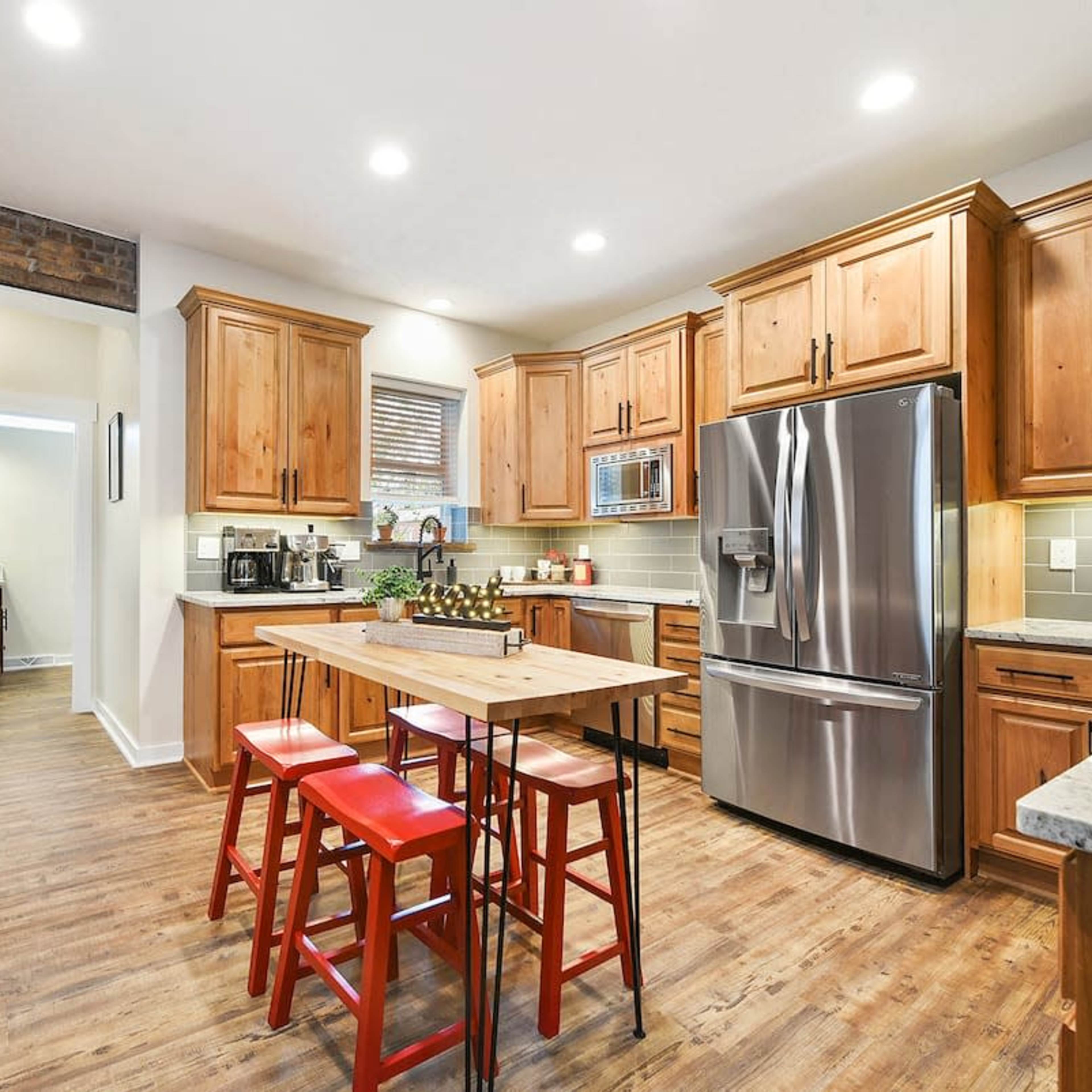 A modern kitchen features wooden cabinetry, stainless steel appliances, and a central island with red stools.