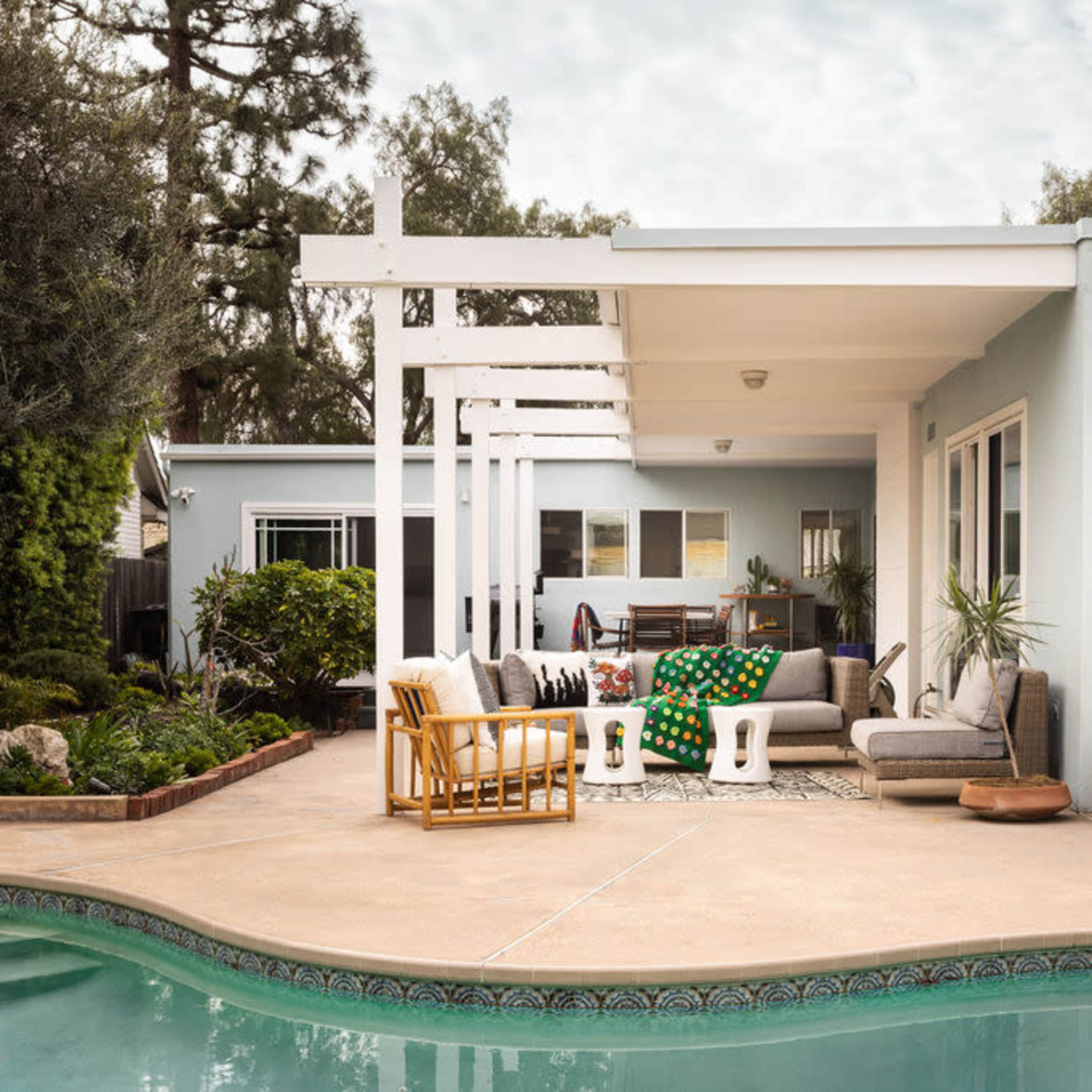 A modern backyard with a swimming pool, featuring a seating area and a house with a light blue exterior.