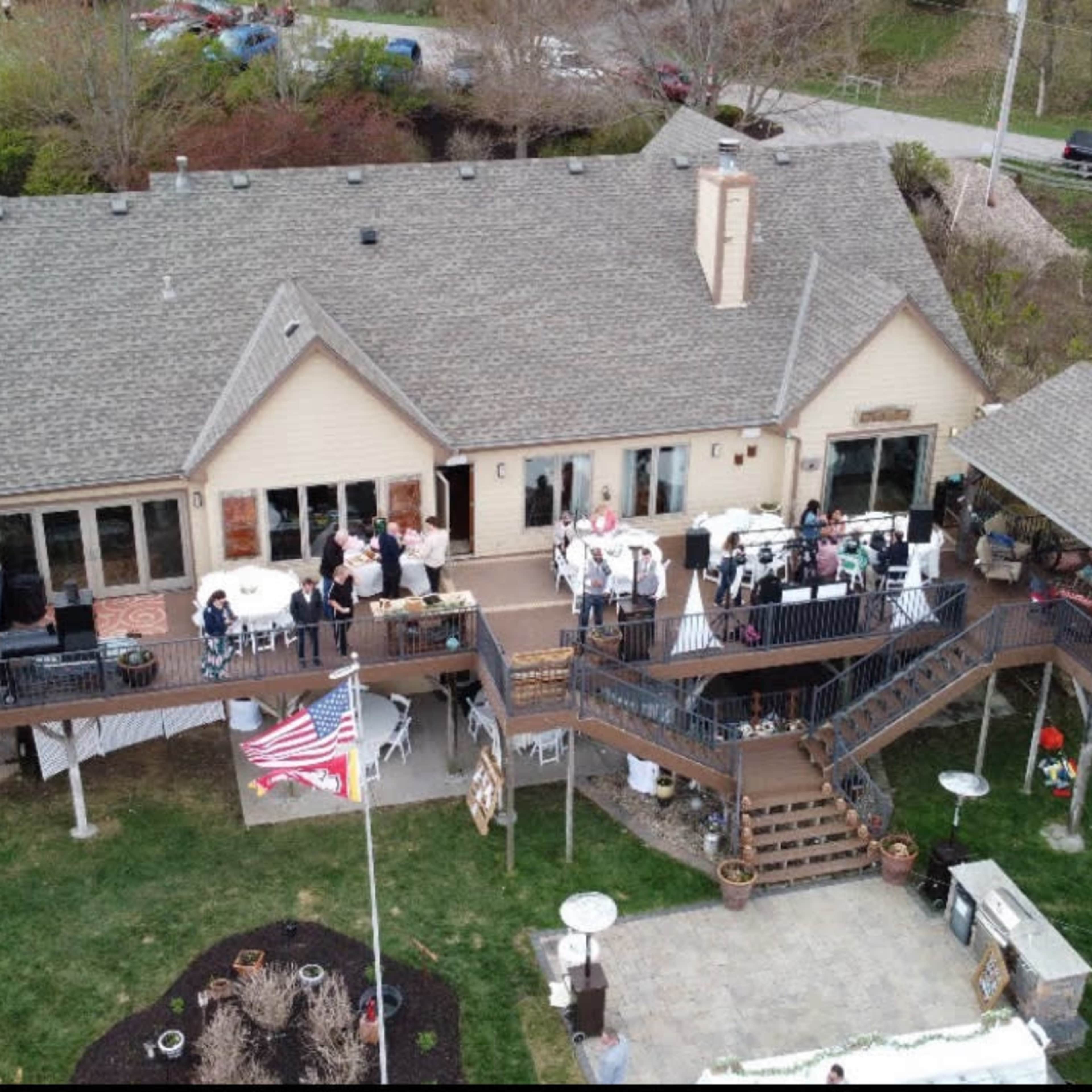 A spacious two-story house with a large deck, where a gathering of people is taking place, along with a well-manicured lawn and various outdoor decorations.