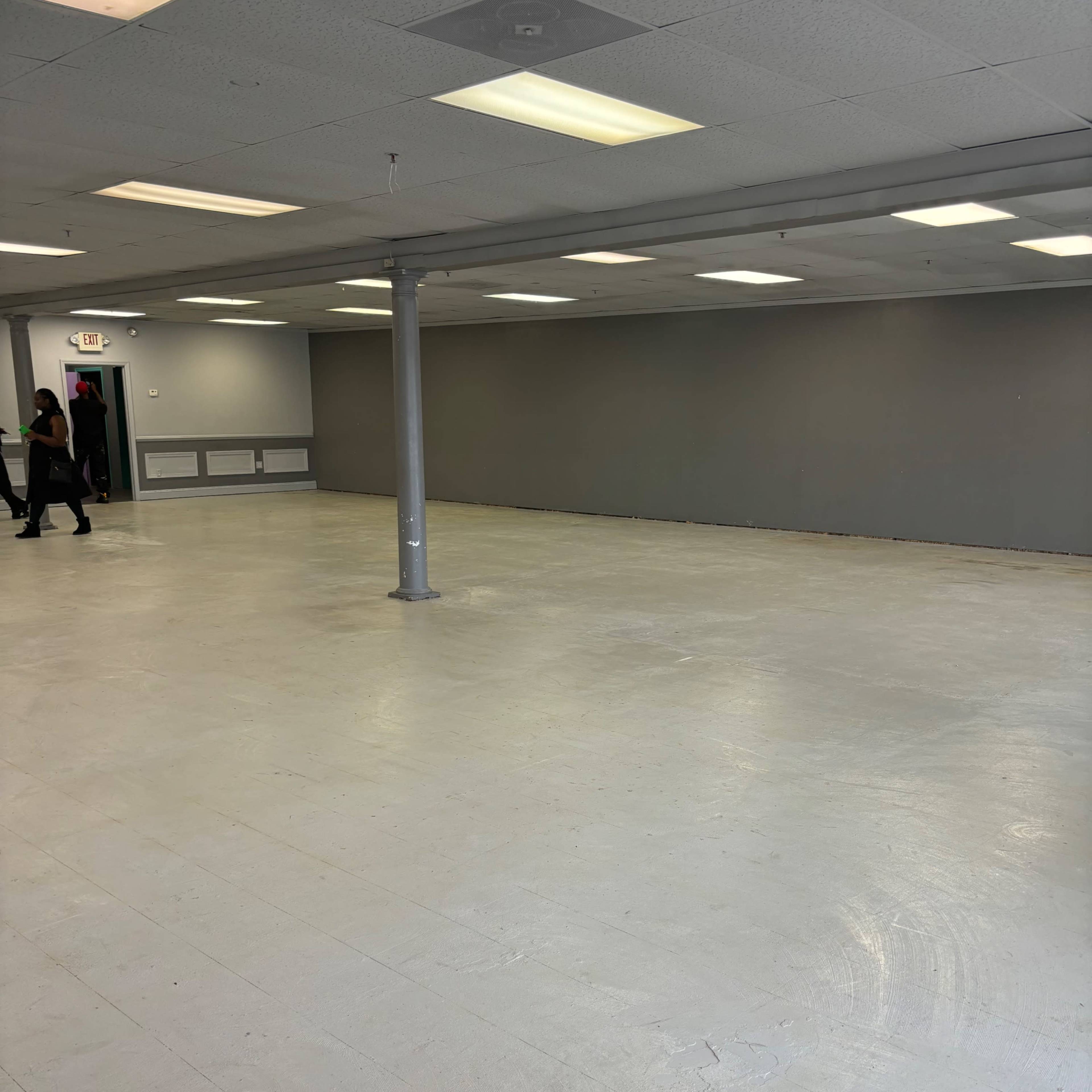 A spacious, empty room with a gray-painted wall, a central support column, and overhead fluorescent lighting.
