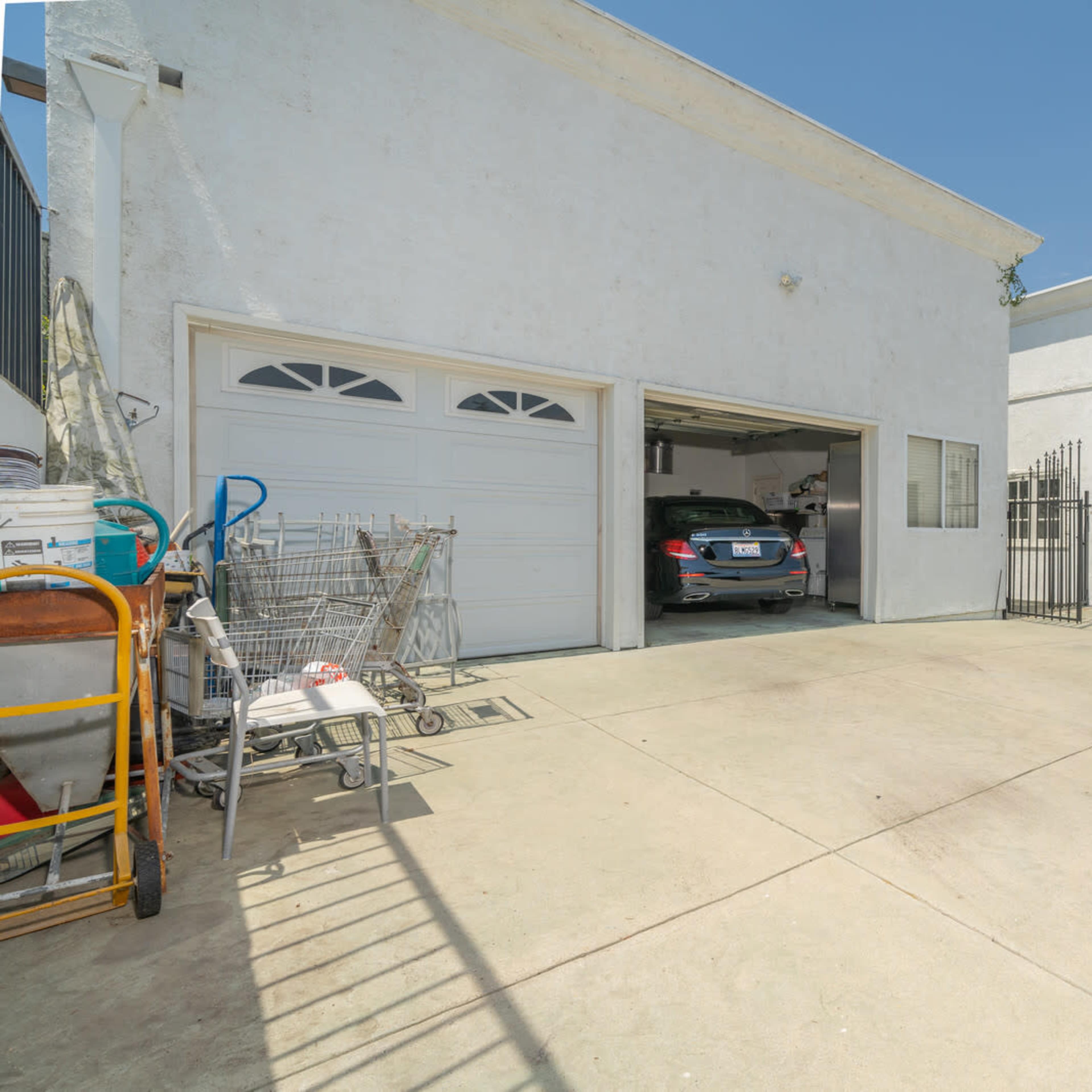 A white building with a garage entrance and a car parked inside, surrounded by a concrete driveway.
