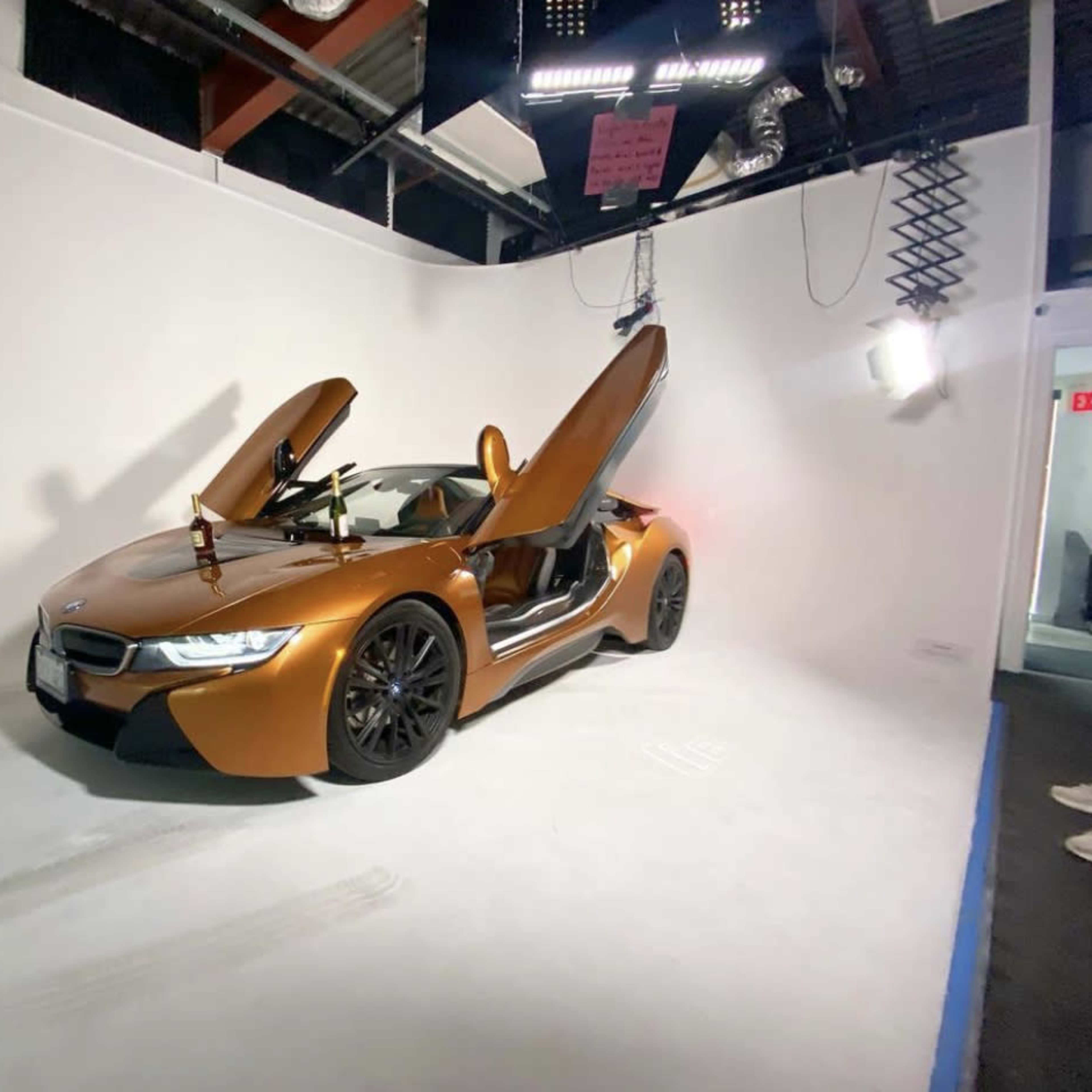 A BMW i8 with its doors open is displayed against a plain white backdrop in a studio setting.
