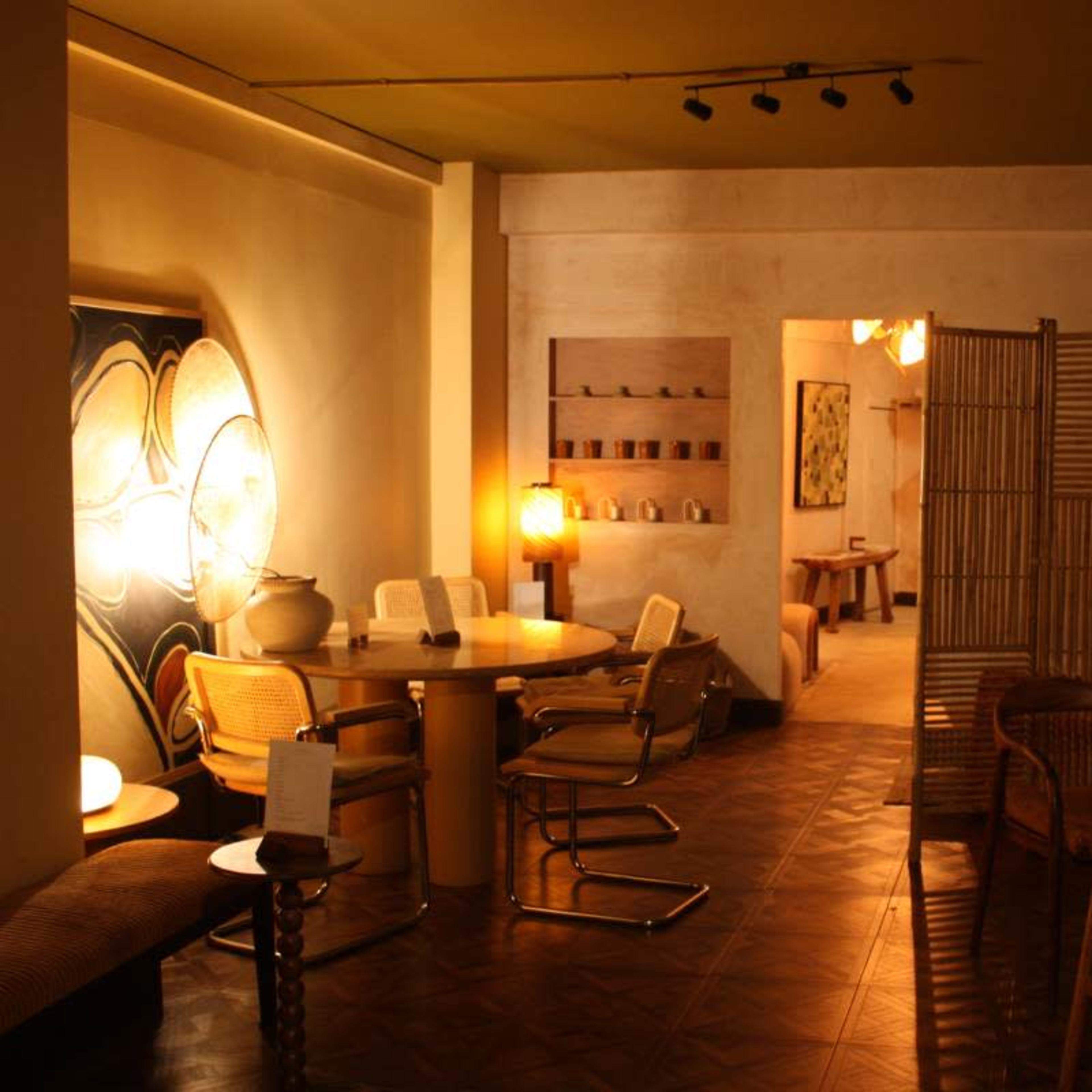 A cozy, minimalist interior space featuring a dining area with a round table and chairs, wooden partitions, and various decorative elements on the walls.