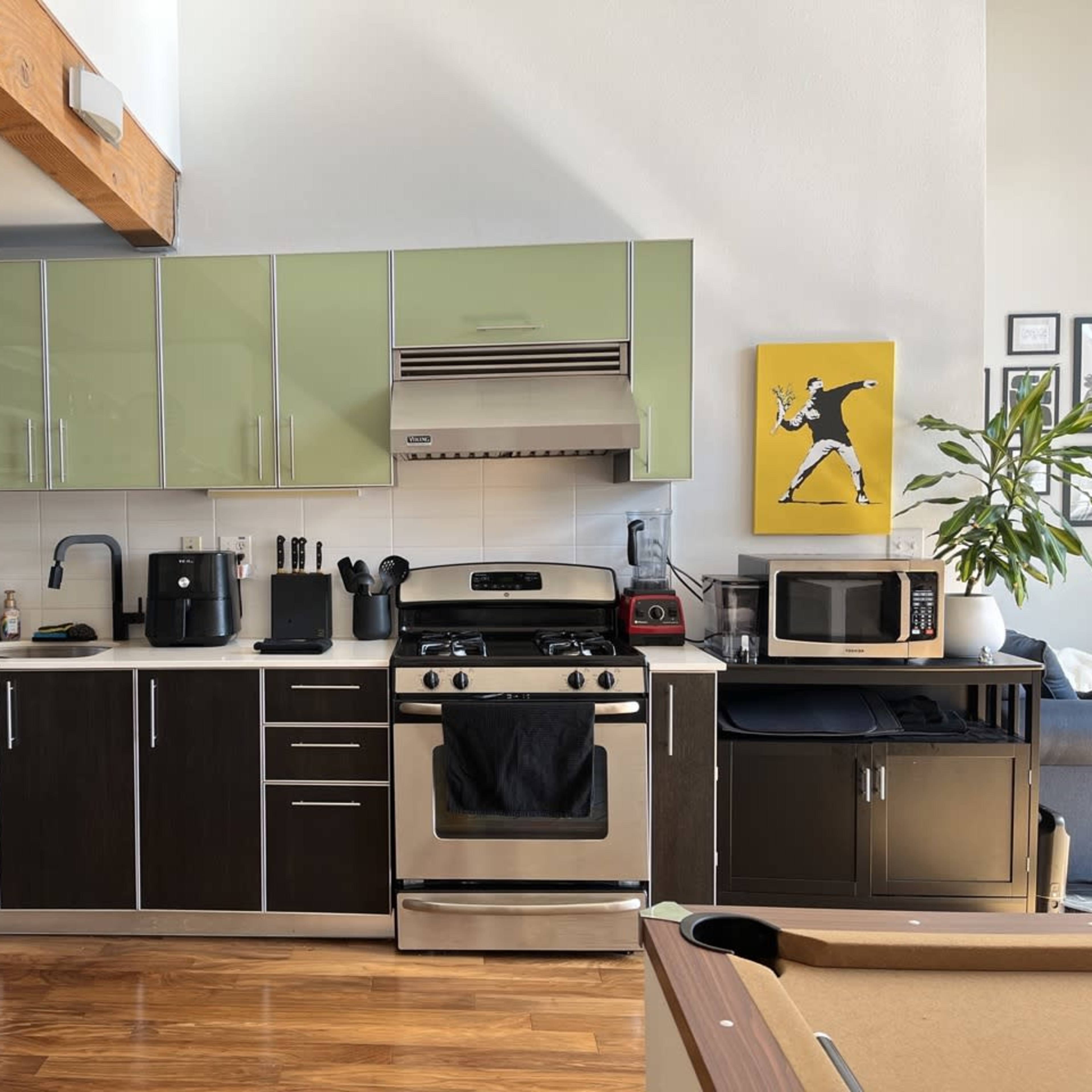 A modern kitchen with green and black cabinetry, featuring a stainless steel stove, microwave, coffee maker, and a large window.