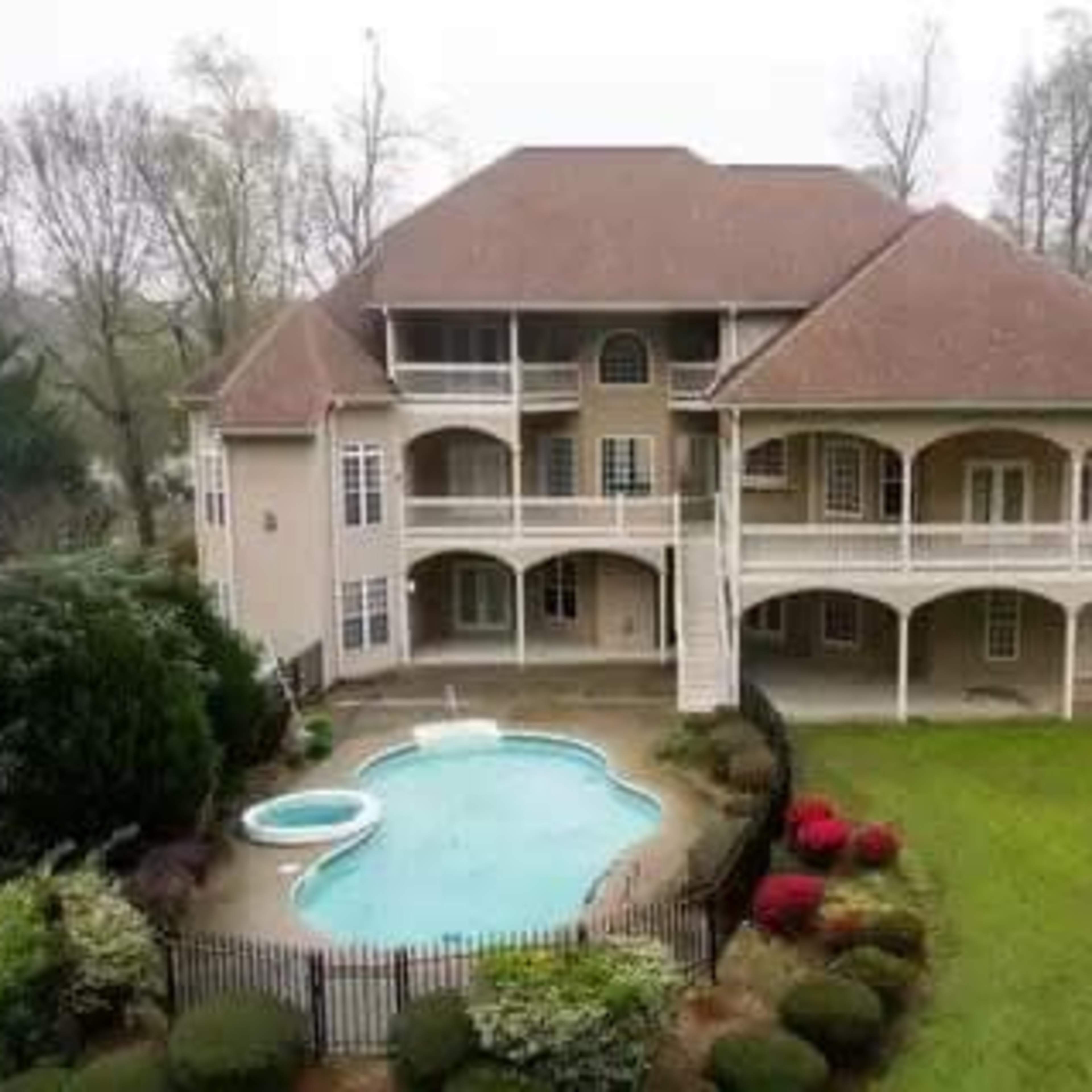 A large multi-story house with a swimming pool and landscaped yard, surrounded by trees.