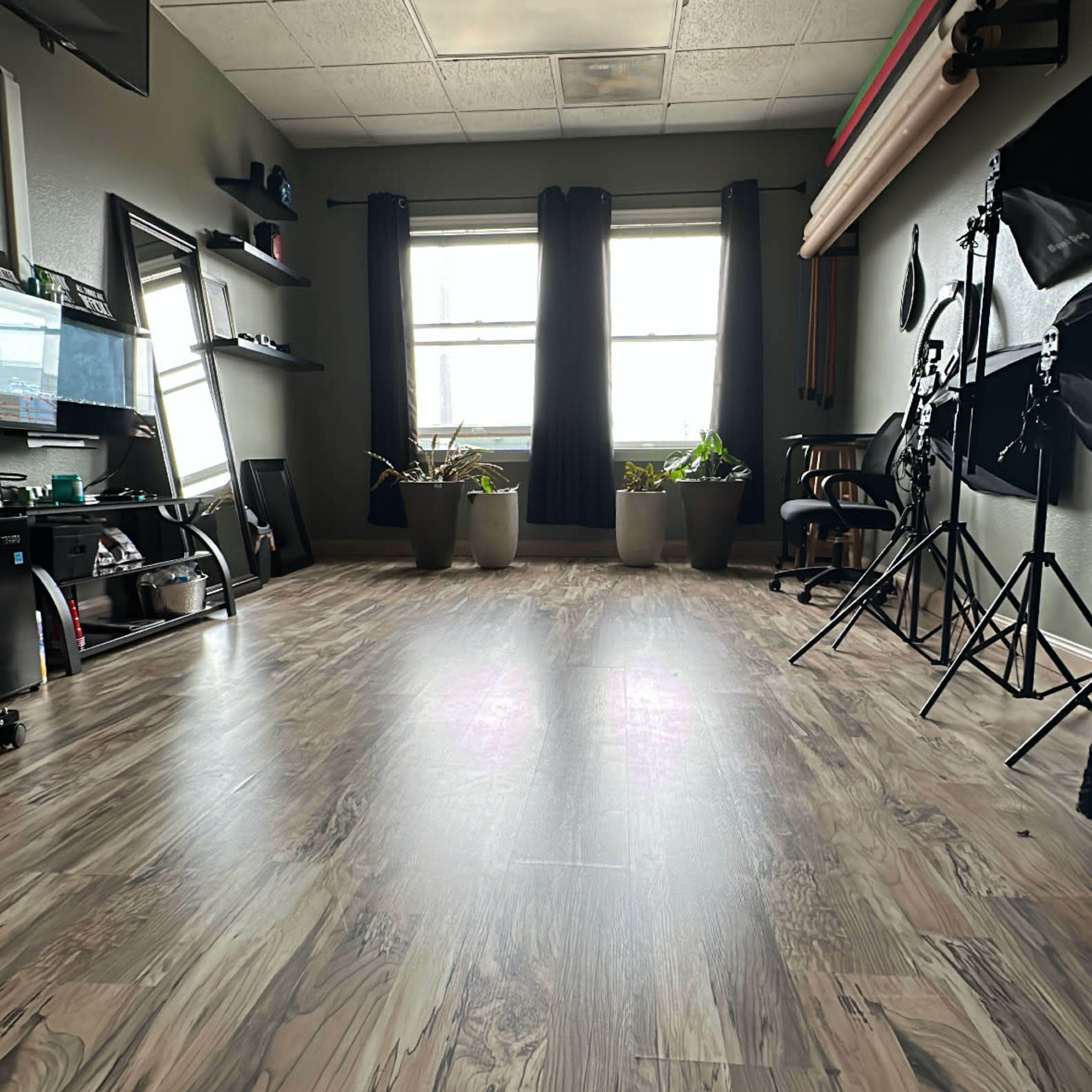 A spacious room with wooden floors, large windows, and various photography equipment along one side.