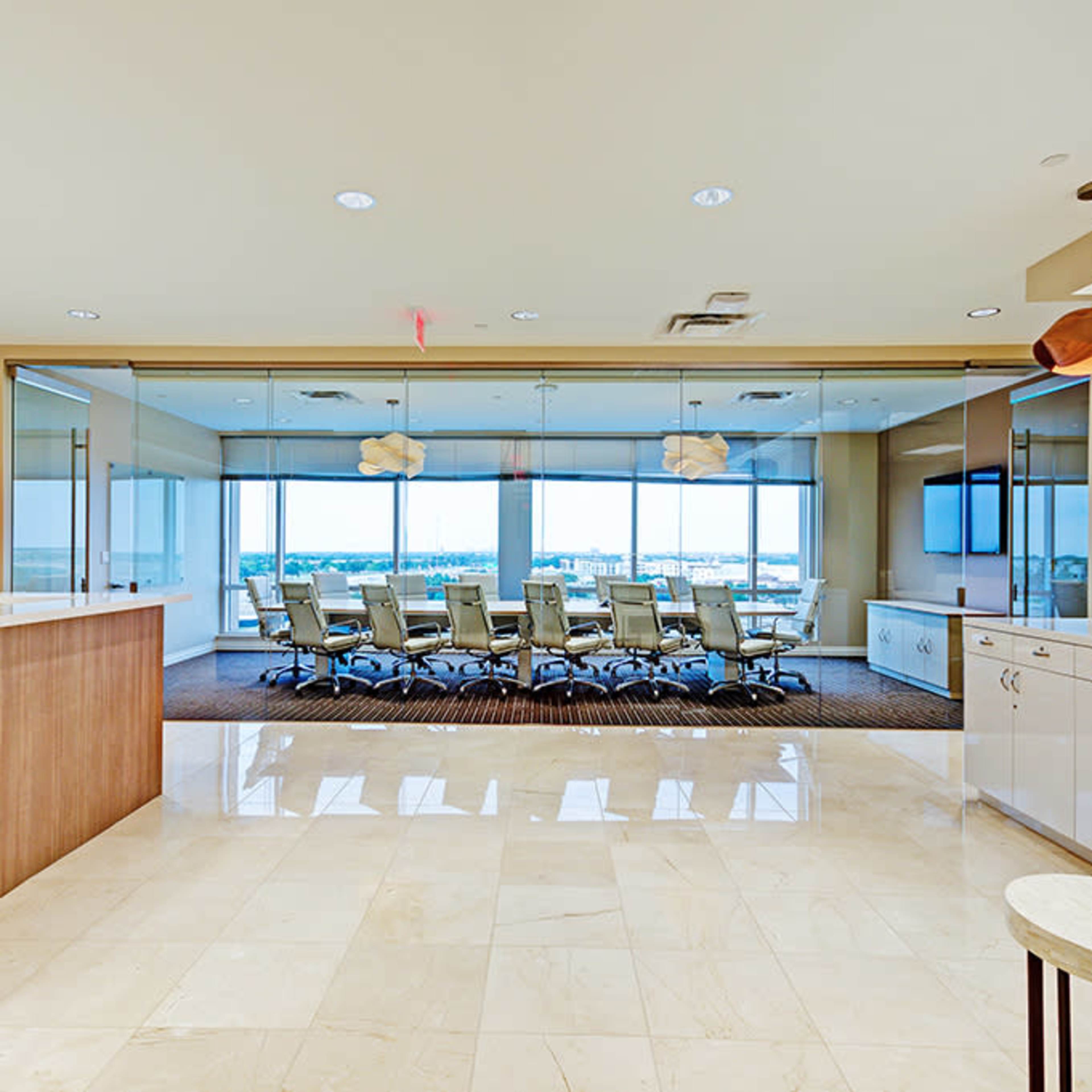 A modern office reception area leading to a conference room with large windows and a long table surrounded by chairs.
