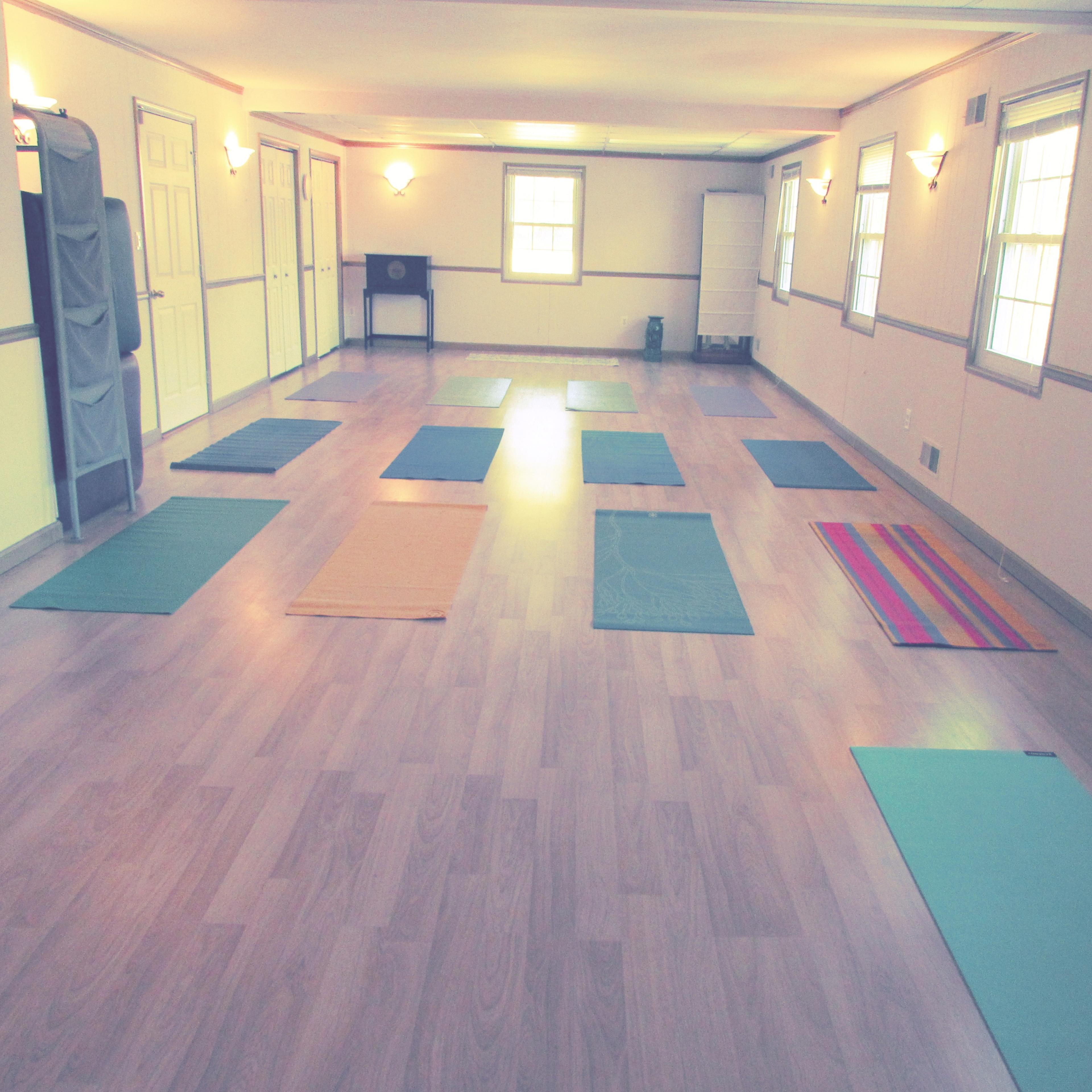 A spacious room with wooden flooring and multiple yoga mats arranged in a grid pattern.