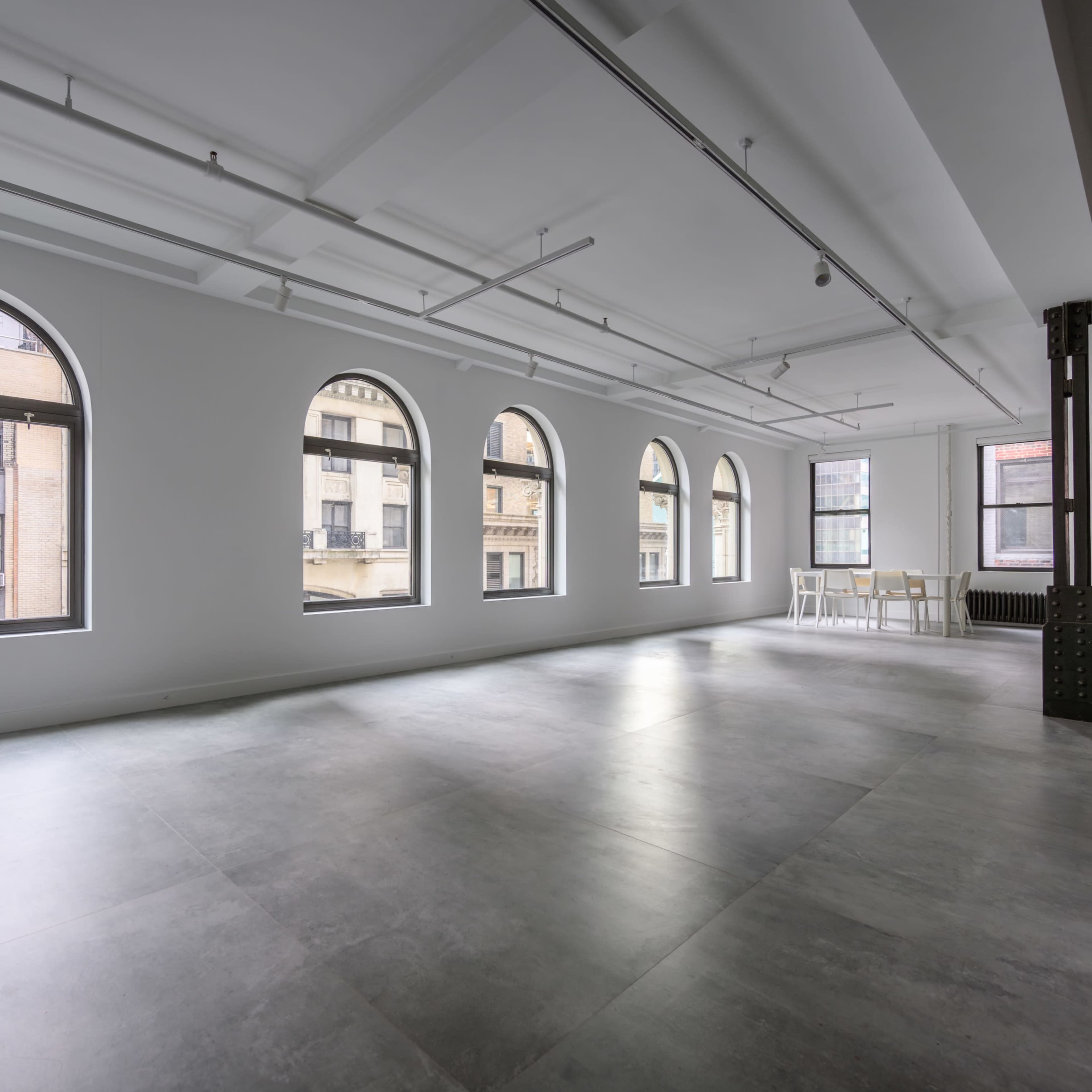 A spacious, empty room with large arched windows and concrete flooring.