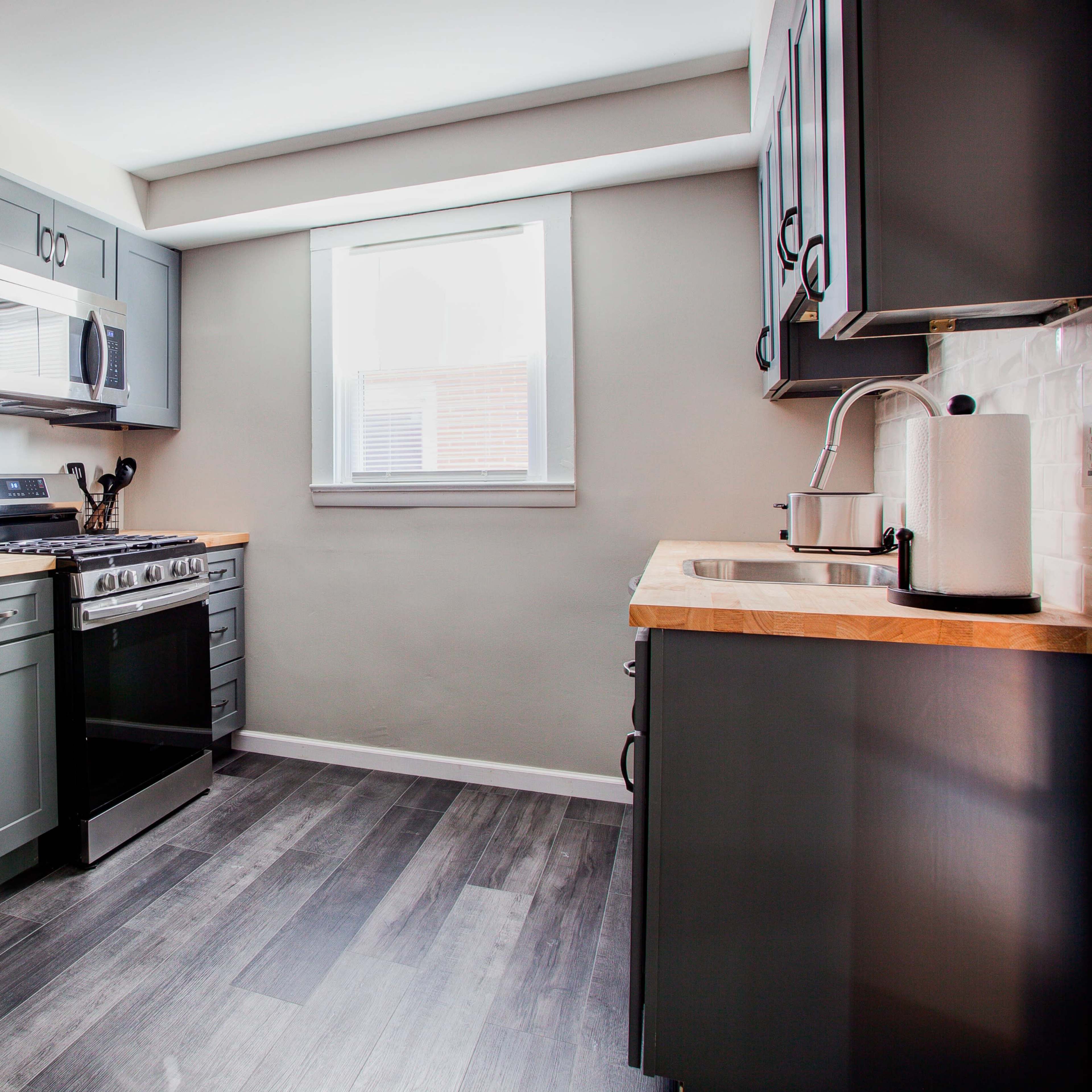A modern kitchen featuring stainless steel appliances, gray cabinetry, and a wooden countertop.