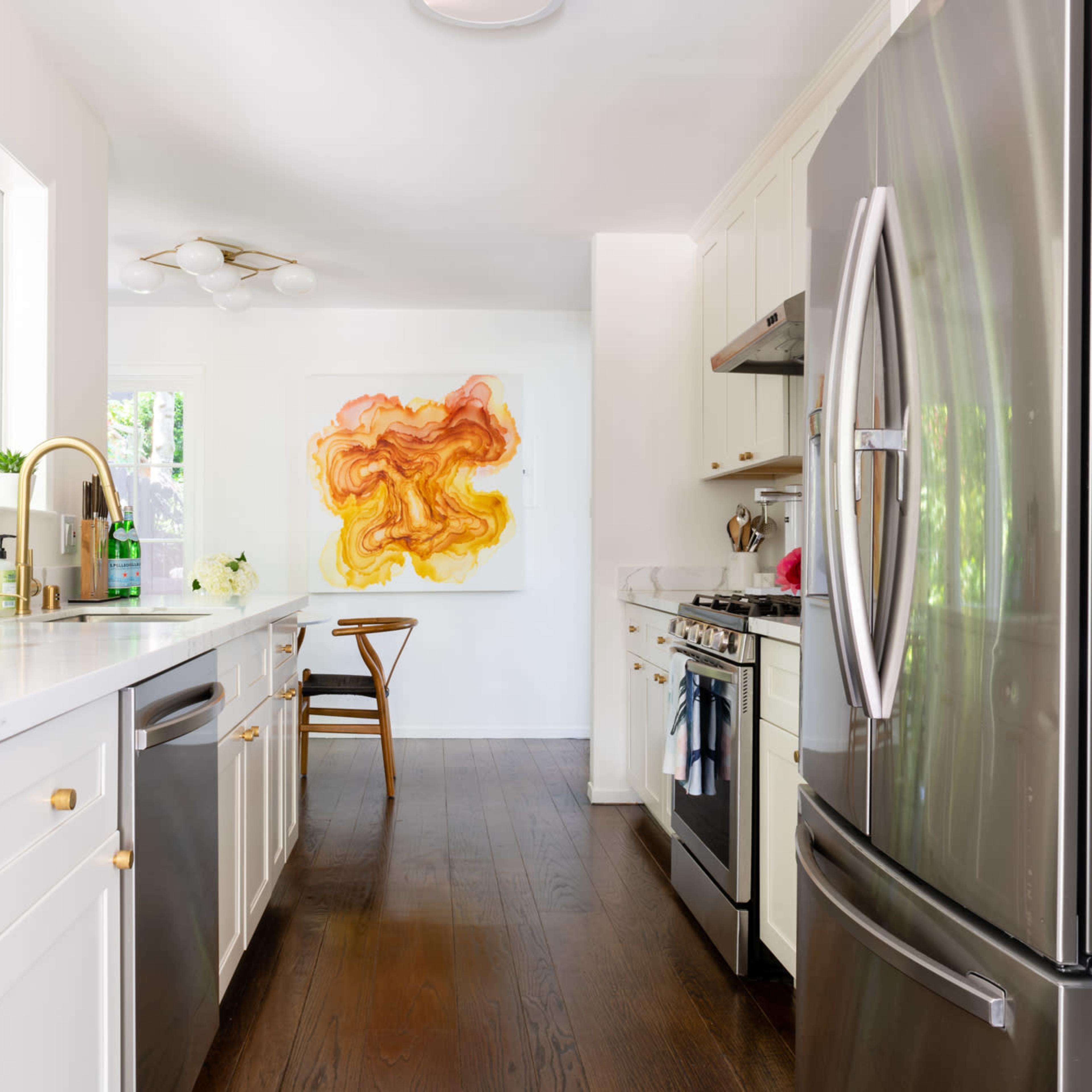 A modern kitchen features stainless steel appliances, white cabinetry, and a colorful abstract painting in the background.
