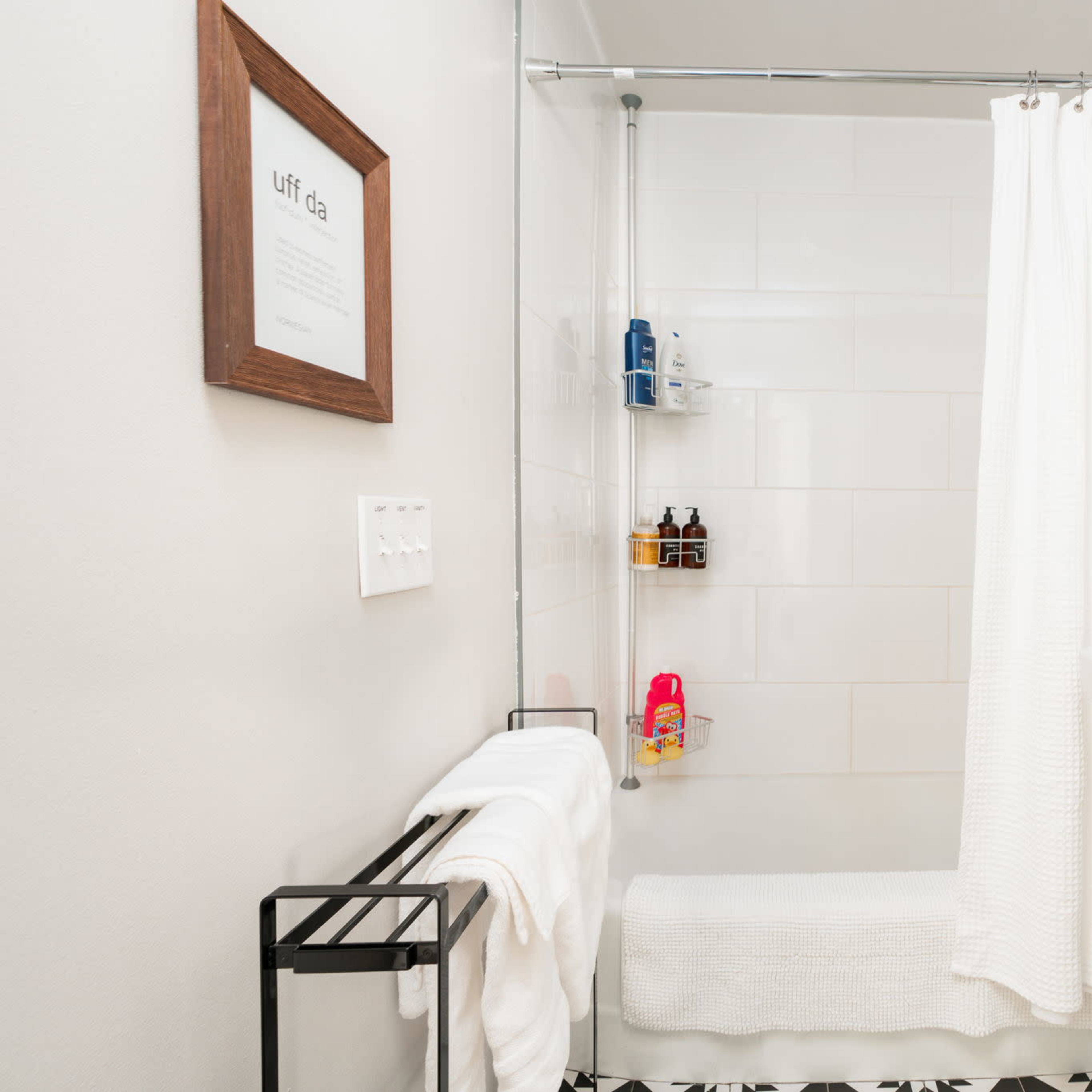 A clean bathroom with a shower area, a sink, a towel rack, and a circular mirror.