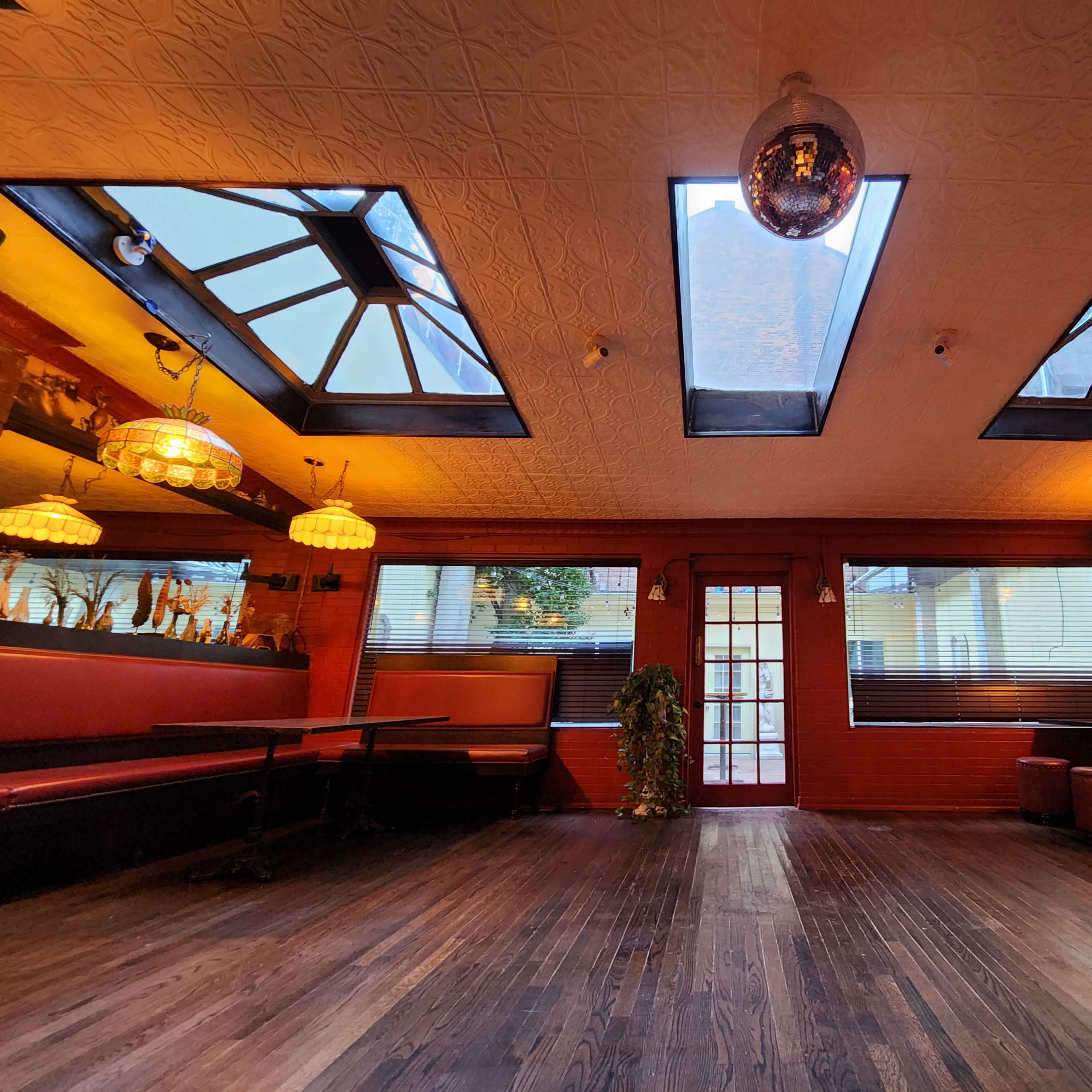 The interior of a restaurant featuring large skylights, red walls, wooden flooring, and a mix of seating arrangements.