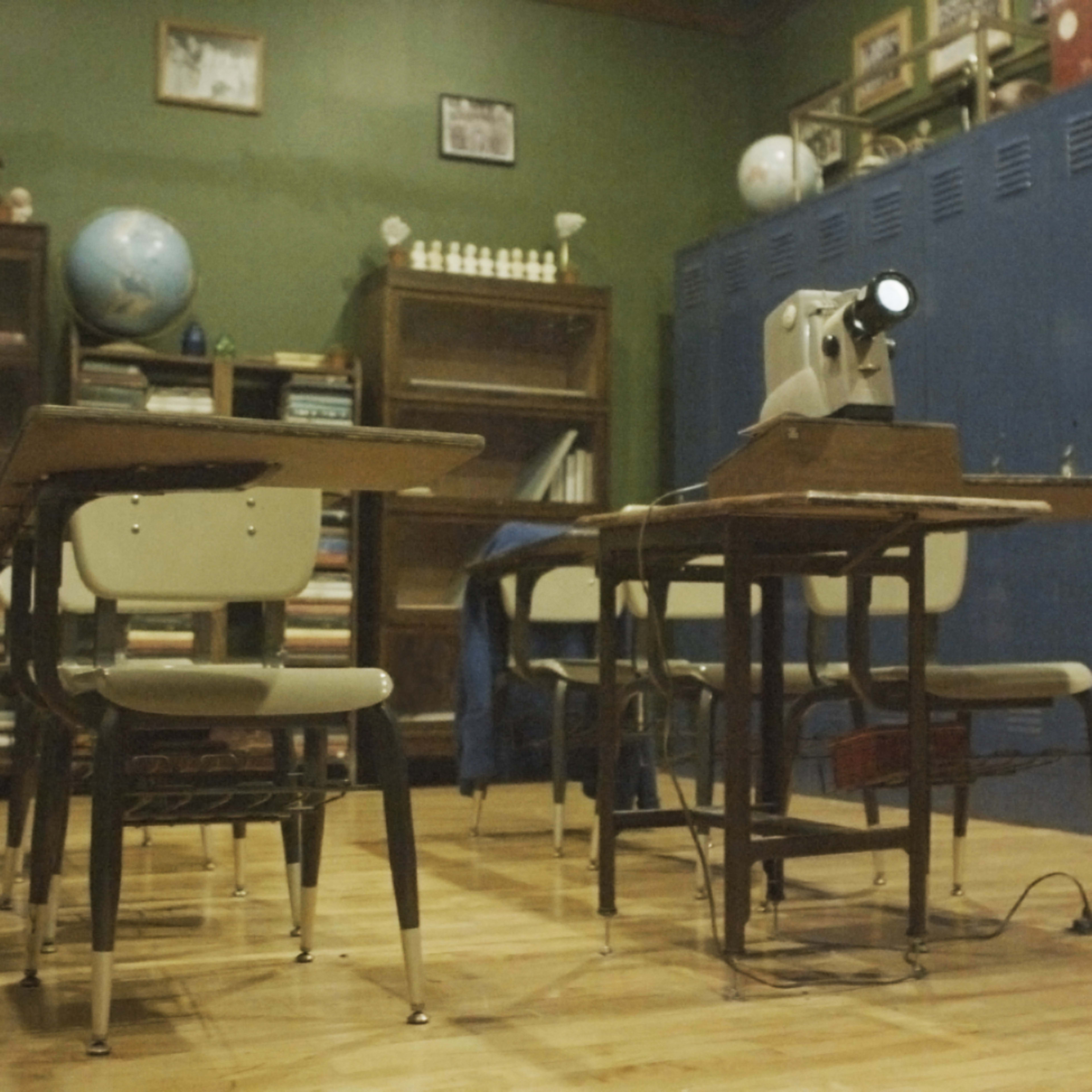 A vintage classroom setup with wooden desks, a globe, a sewing machine, and shelves filled with books.