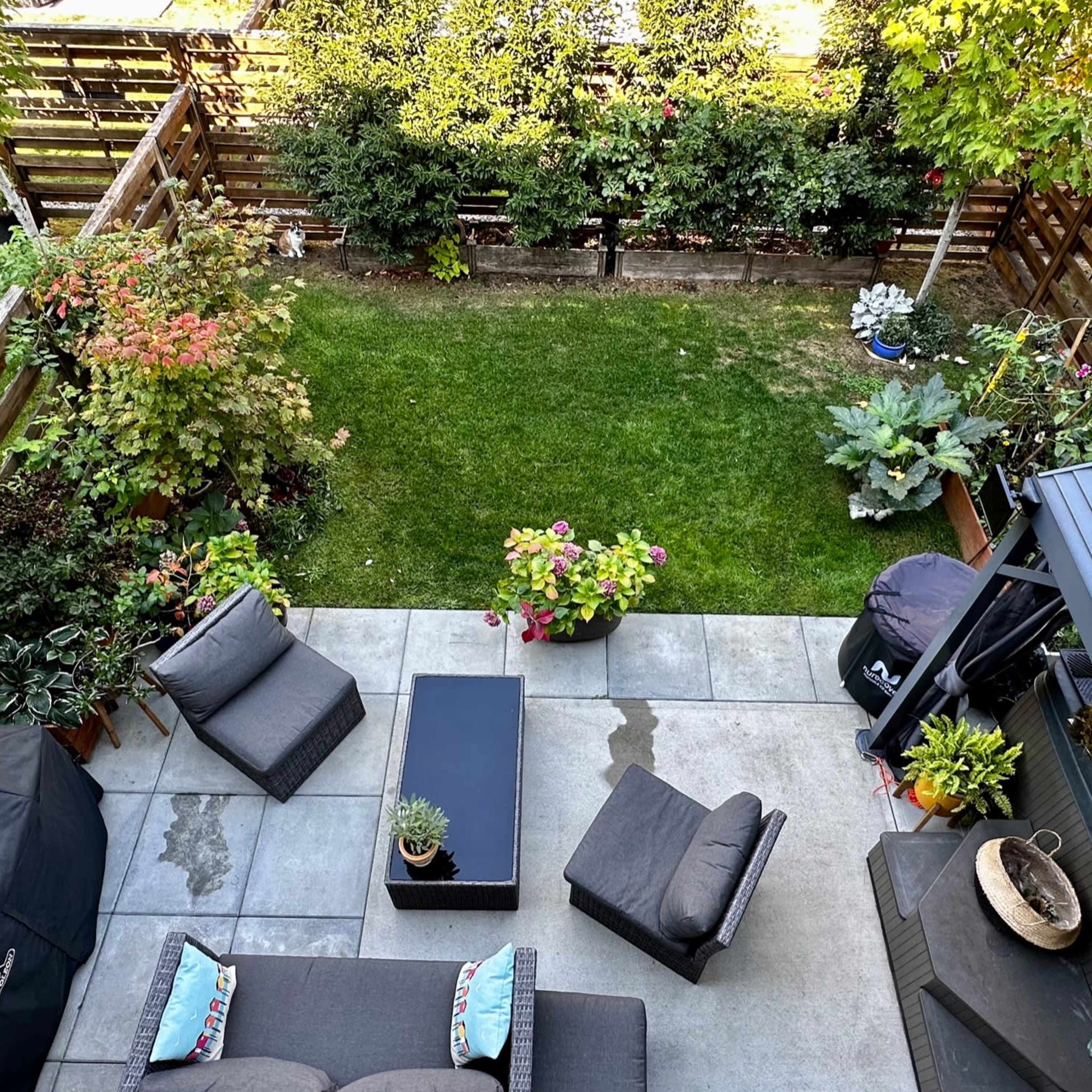 A neatly arranged outdoor patio with gray furniture, surrounded by greenery and a well-maintained lawn.