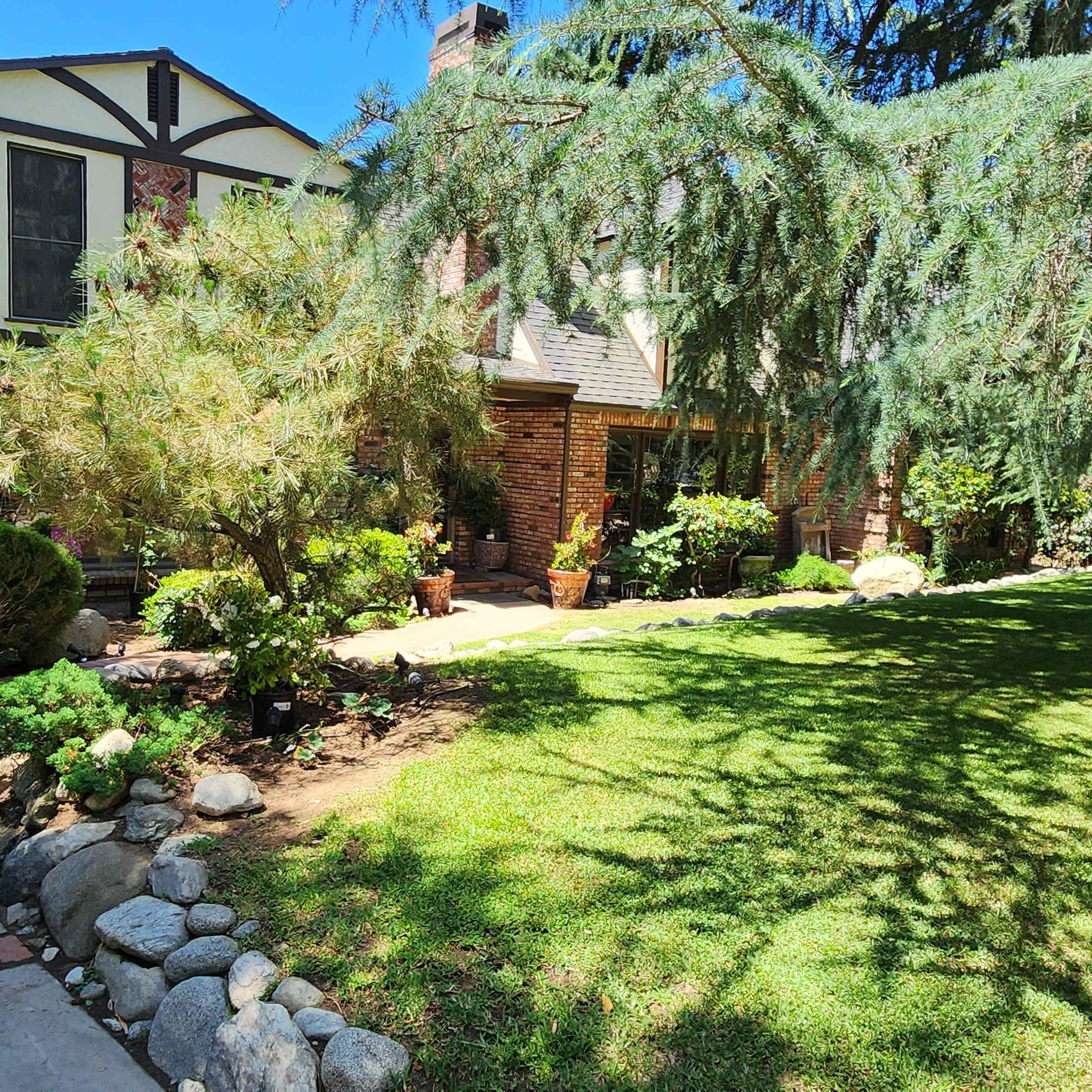 A brick house with a sloped roof, surrounded by greenery and a pathway leading to the entrance.