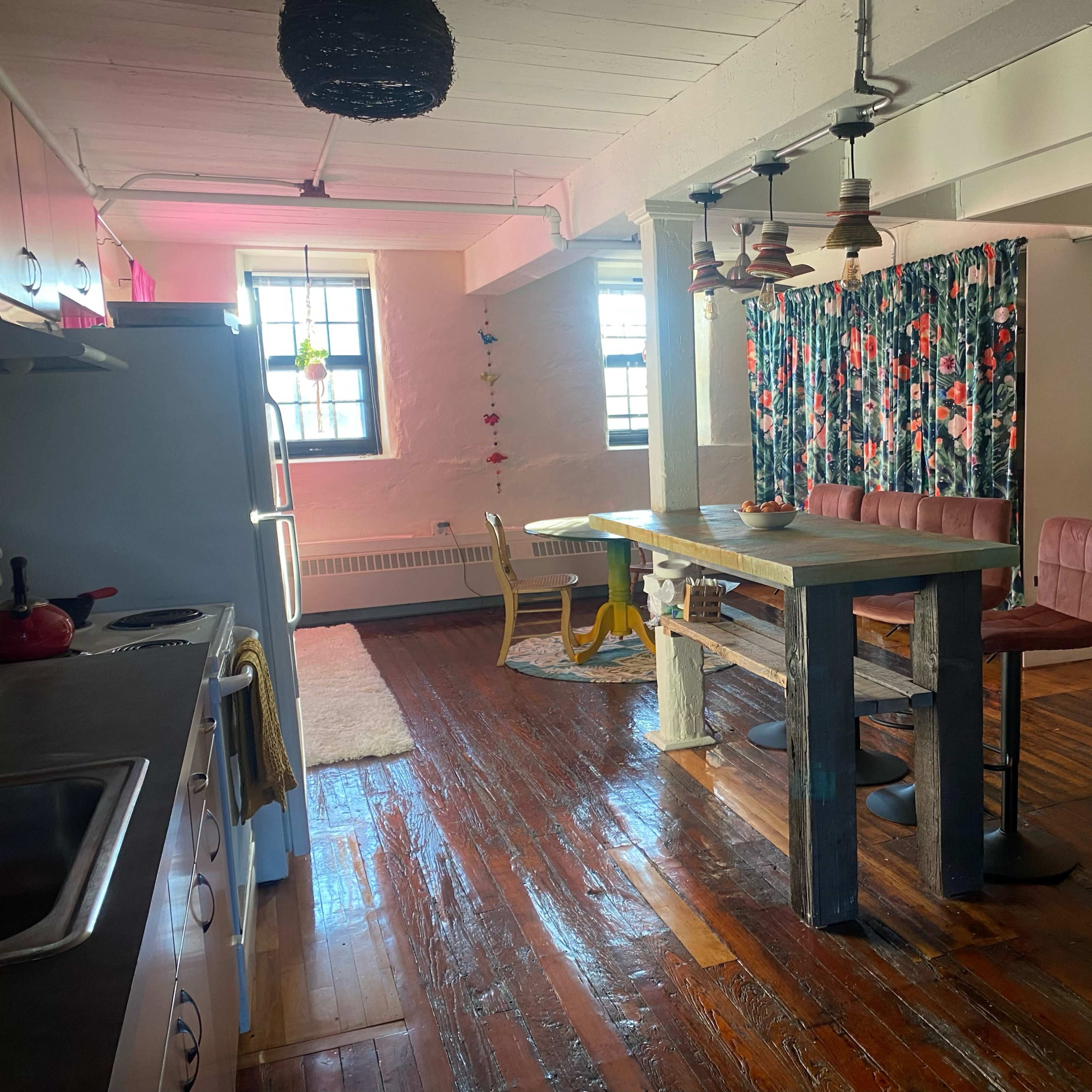 A spacious interior with a kitchen area on the left, a dining table in the center, and a decorated wall with colorful artwork in the background.