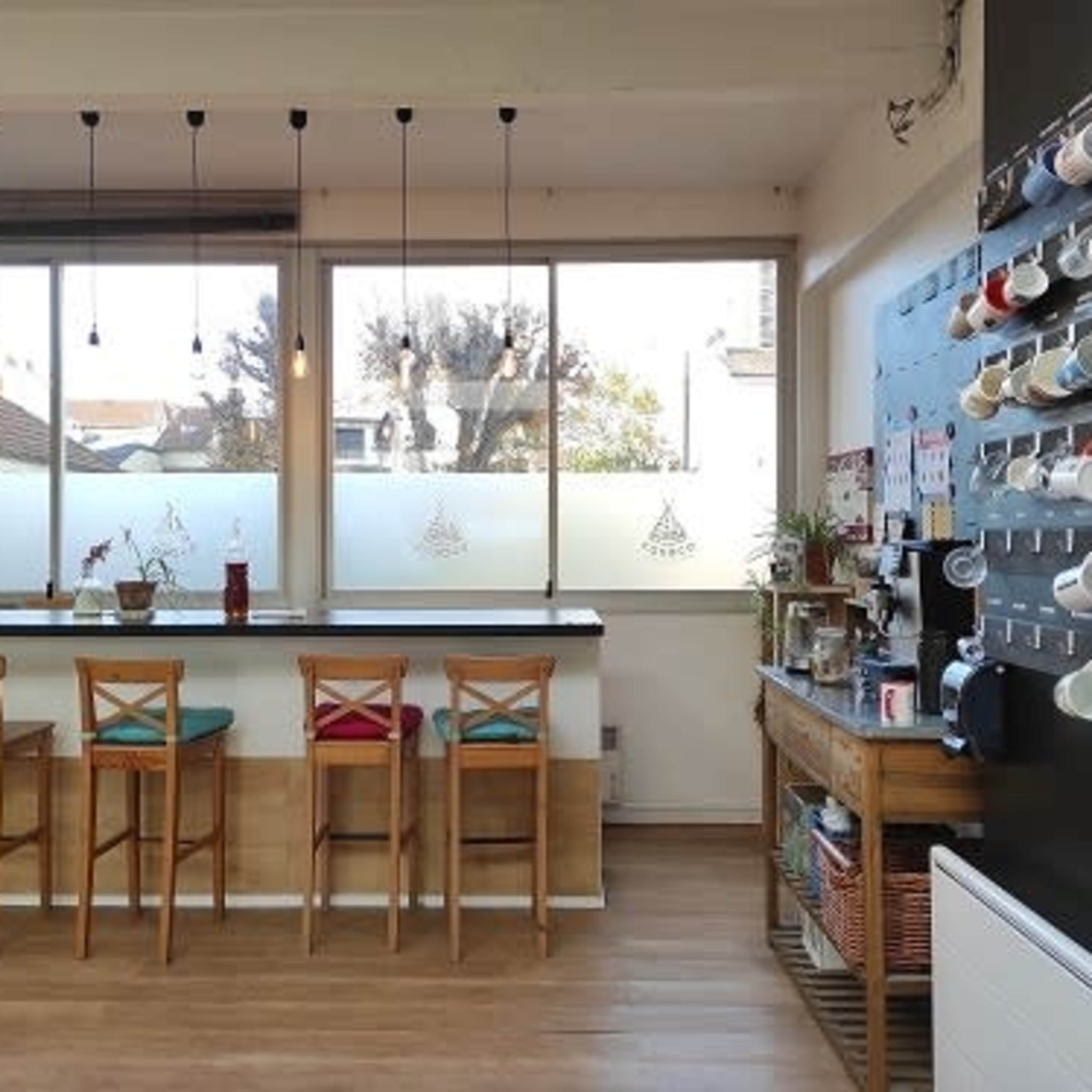 A modern café interior with a bar area featuring wooden stools, a counter with beverages, and a wall displaying various coffee mugs.