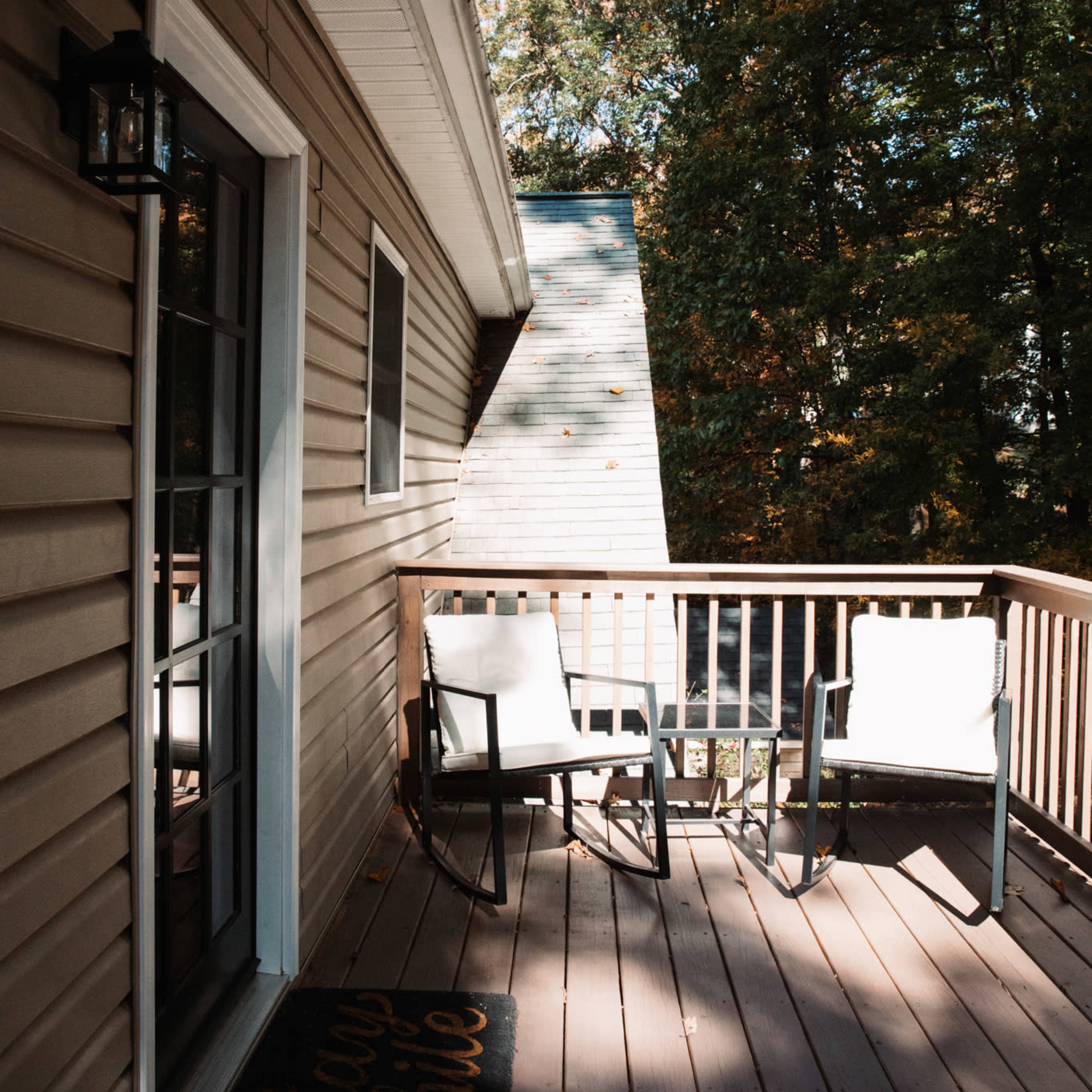 A wooden deck with two chairs overlooks a tree-filled backyard on a clear day.