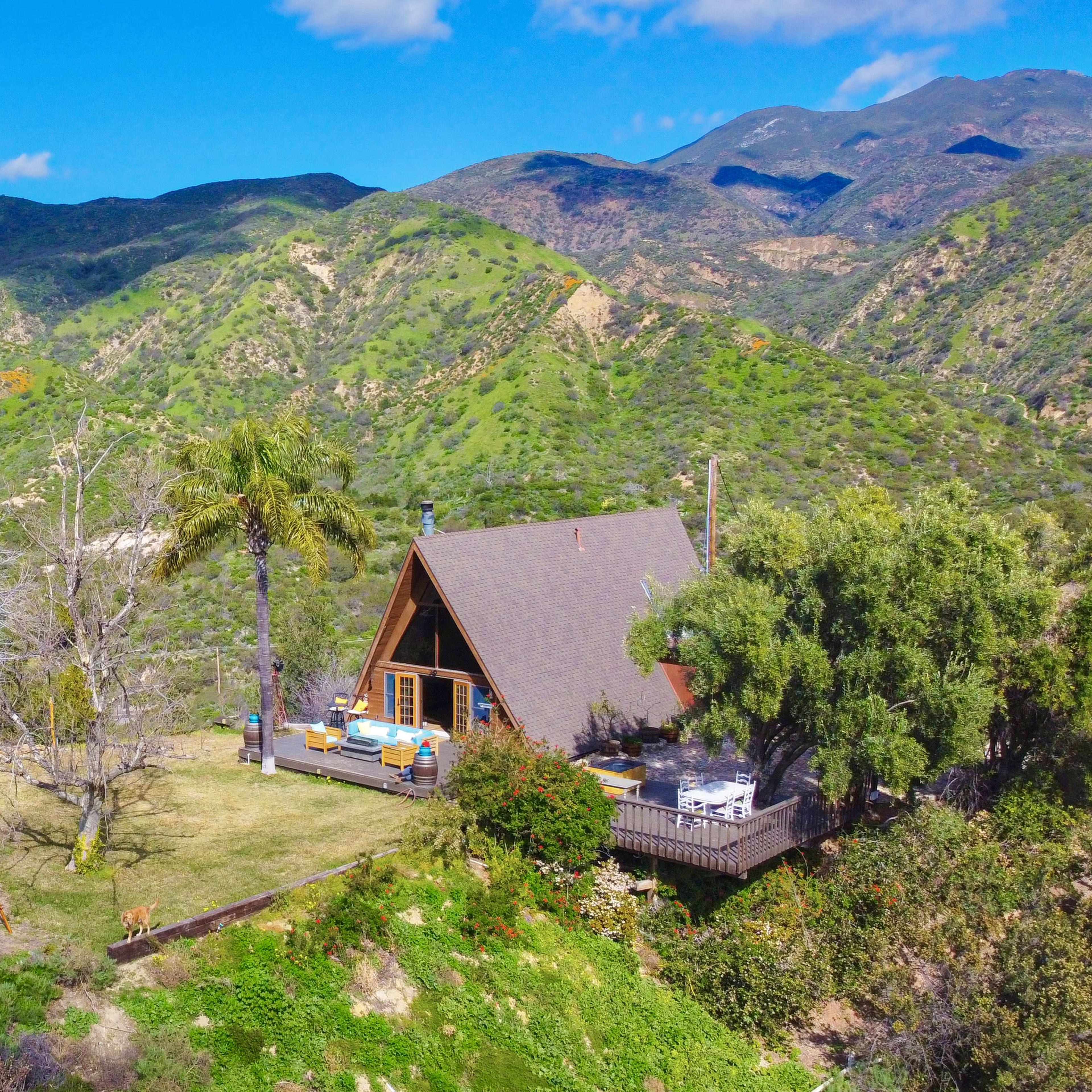 A cabin is situated on a grassy area surrounded by mountains and lush greenery.