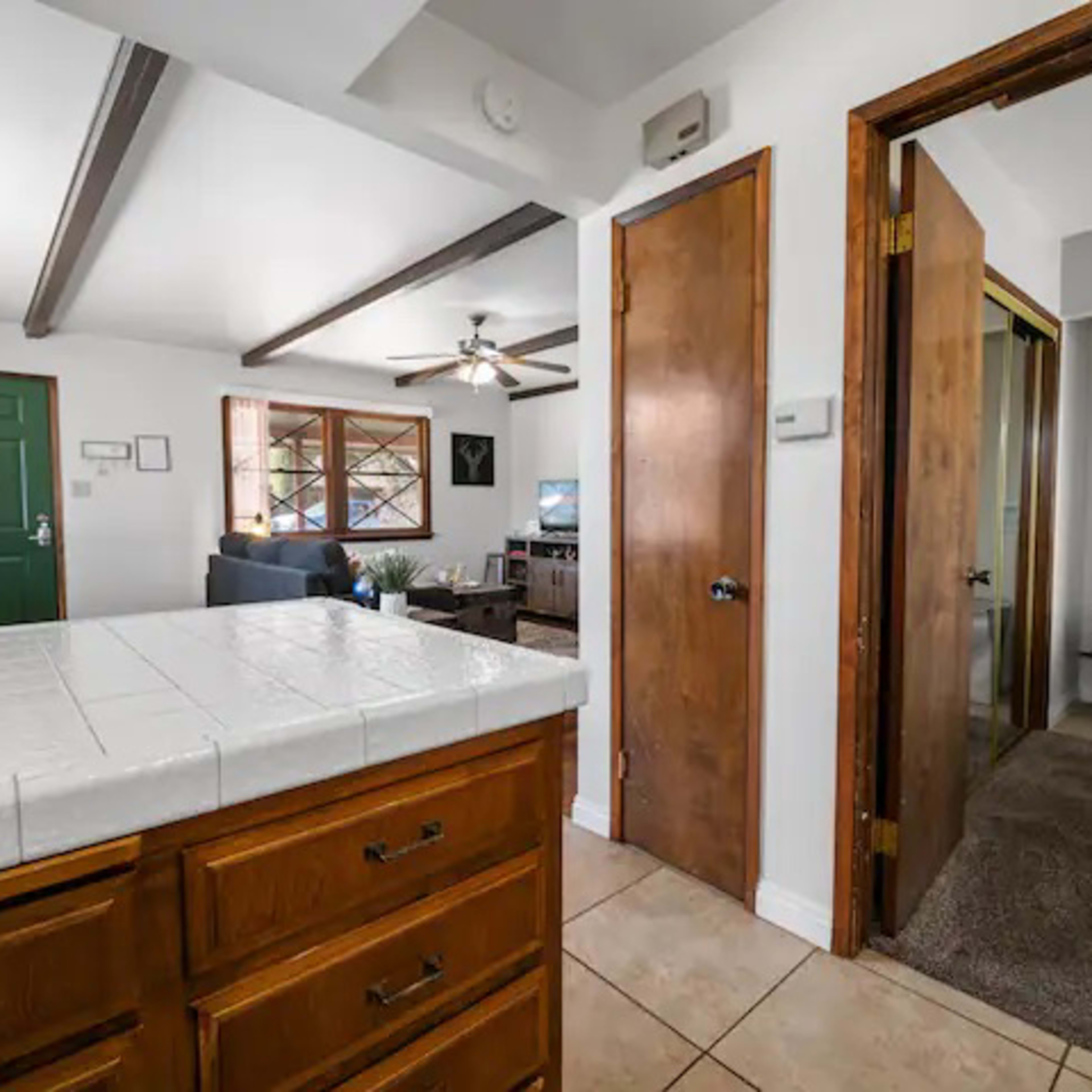 A view of a home's interior, featuring a kitchen with wooden cabinets, a doorway leading to a hallway, and an adjacent living area with a television.