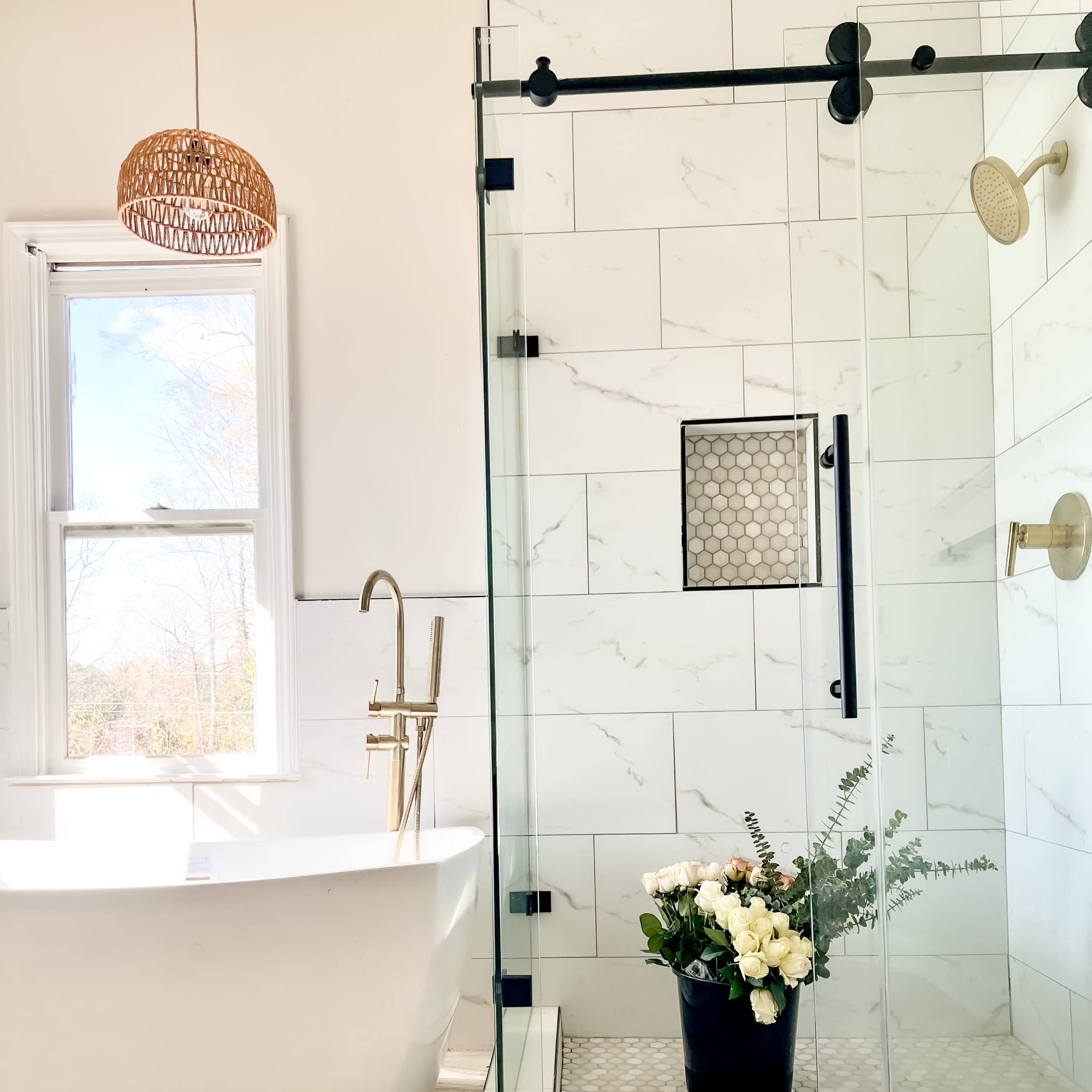 A modern bathroom with a freestanding tub on one side and a glass shower enclosure featuring a floral arrangement on the floor inside.