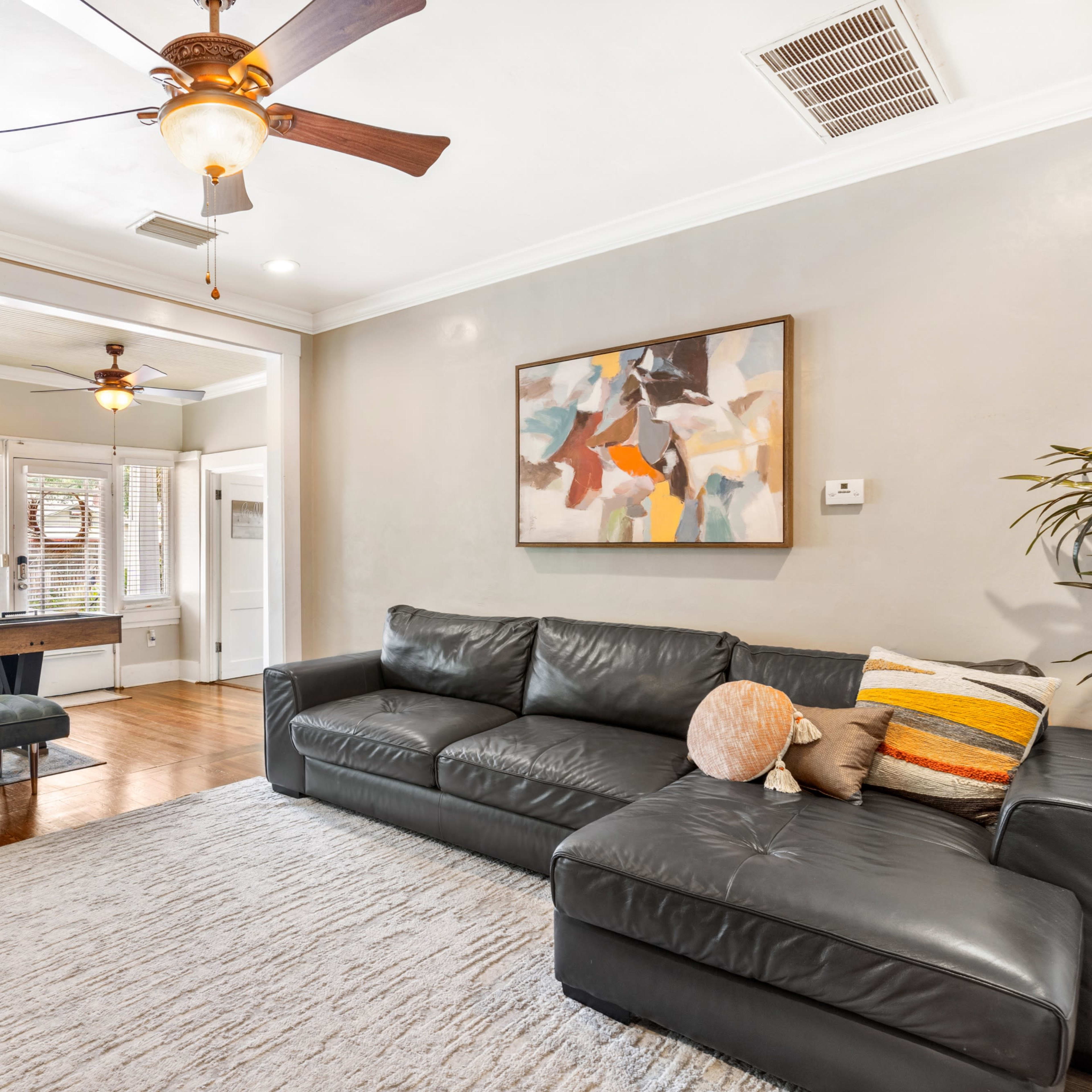 A living room with a black leather sectional sofa, a coffee table, a desk area with a window, and two ceiling fans.