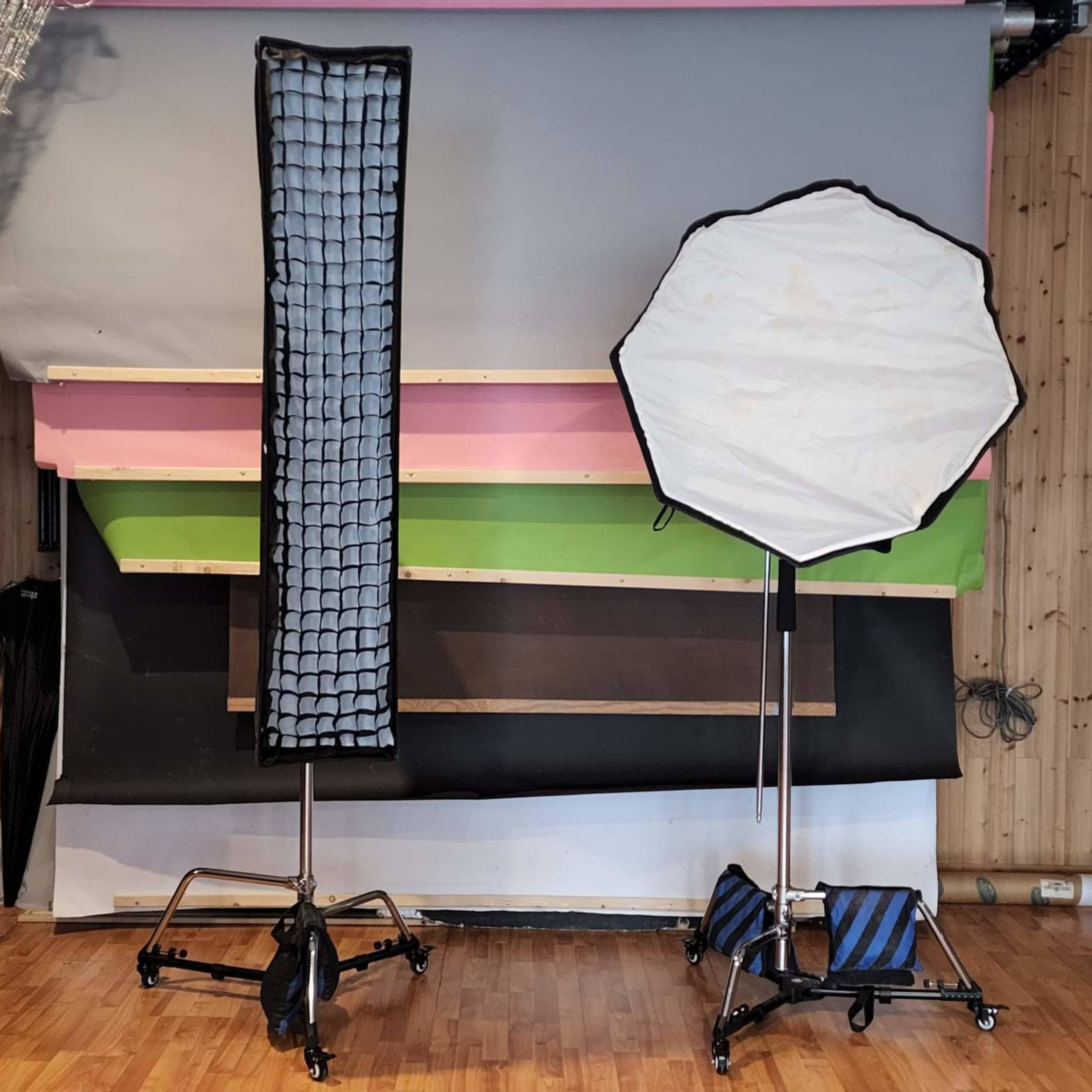 A photography studio setup with a softbox and a grid reflector on stands, positioned in front of a colorful backdrop.