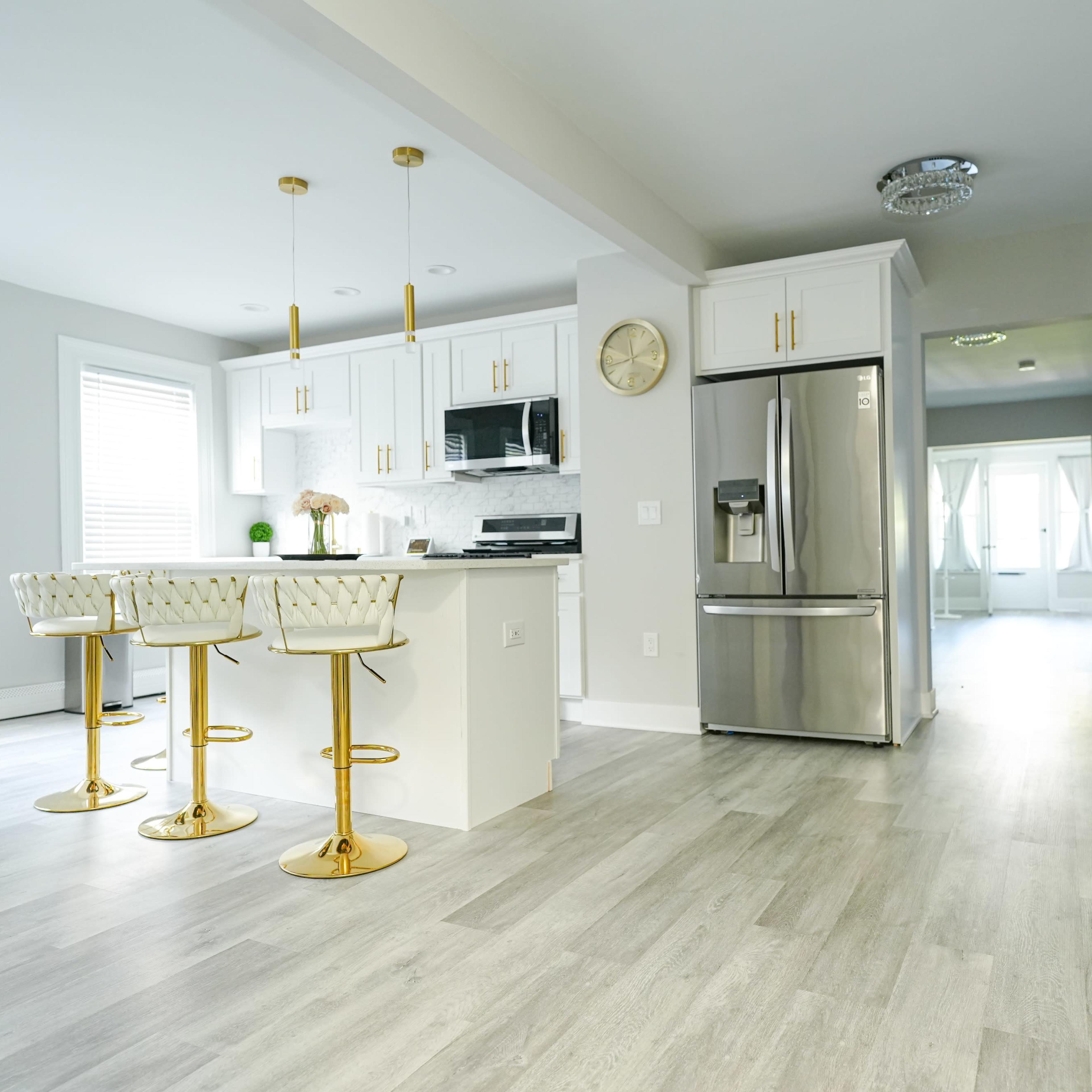 A modern kitchen with white cabinetry, stainless steel appliances, and gold-accented bar stools around a central island.