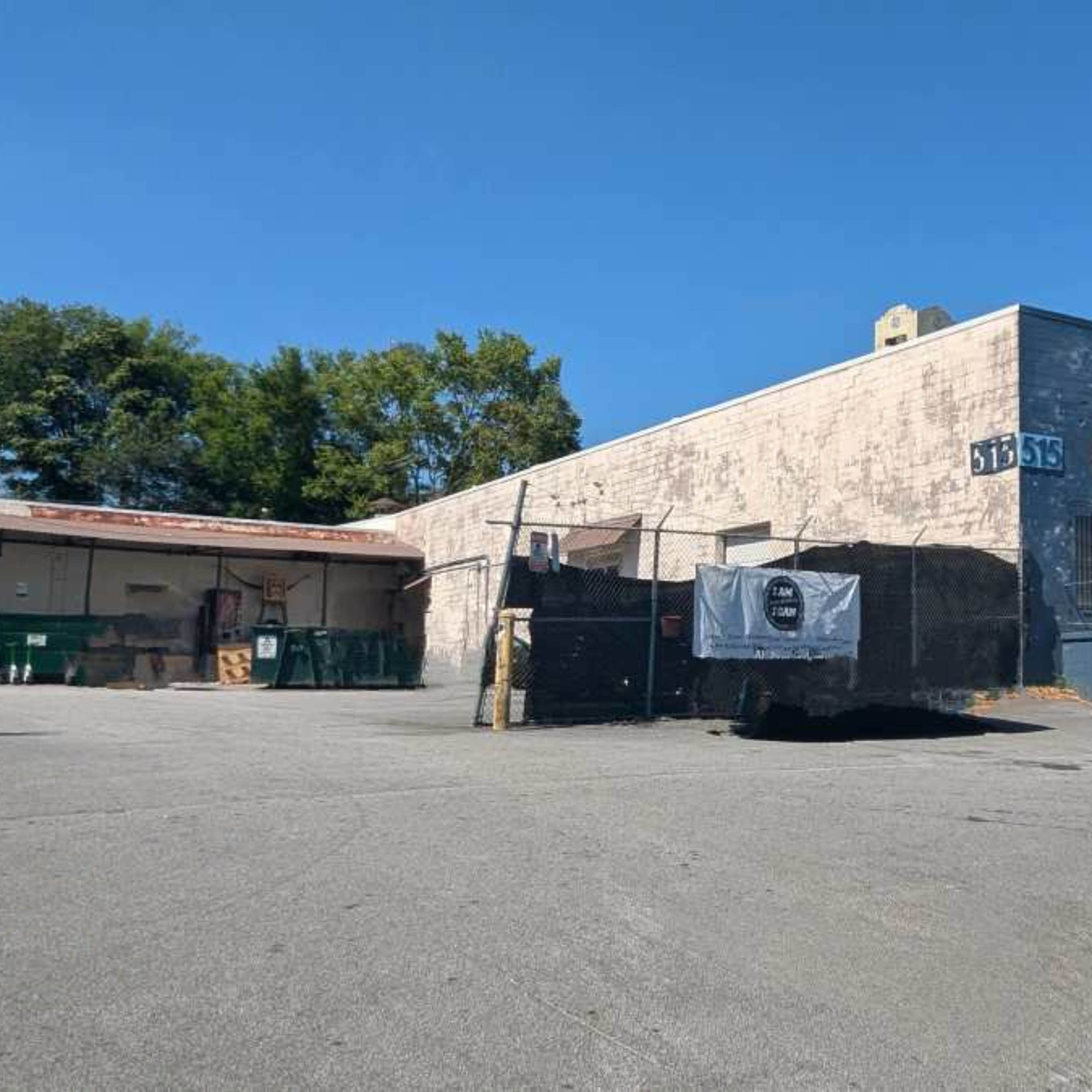 A vacant lot with a large, faded building featuring a mural of a vintage vehicle on its side.