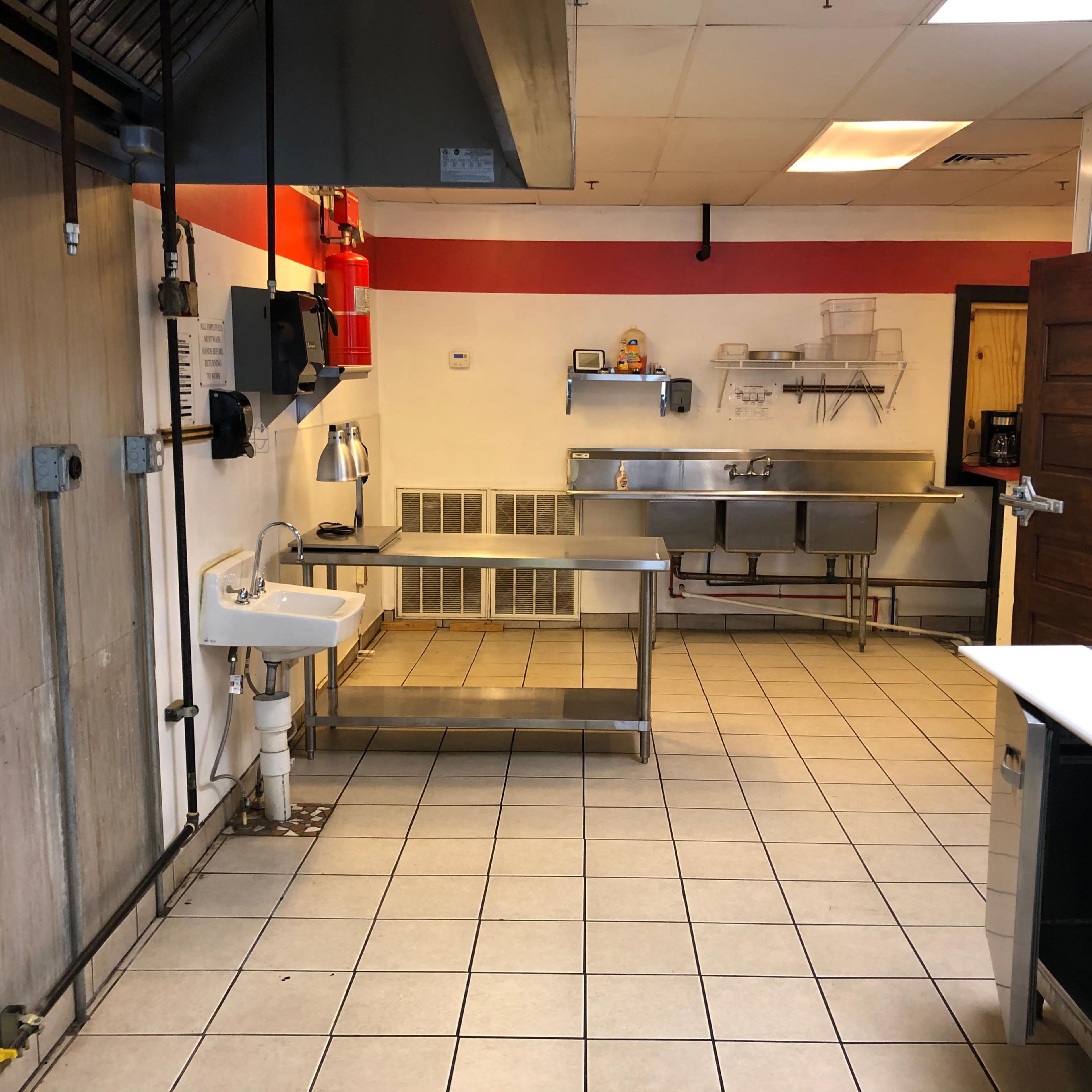 A commercial kitchen with stainless steel worktables, a sink, and various kitchen equipment against the walls.
