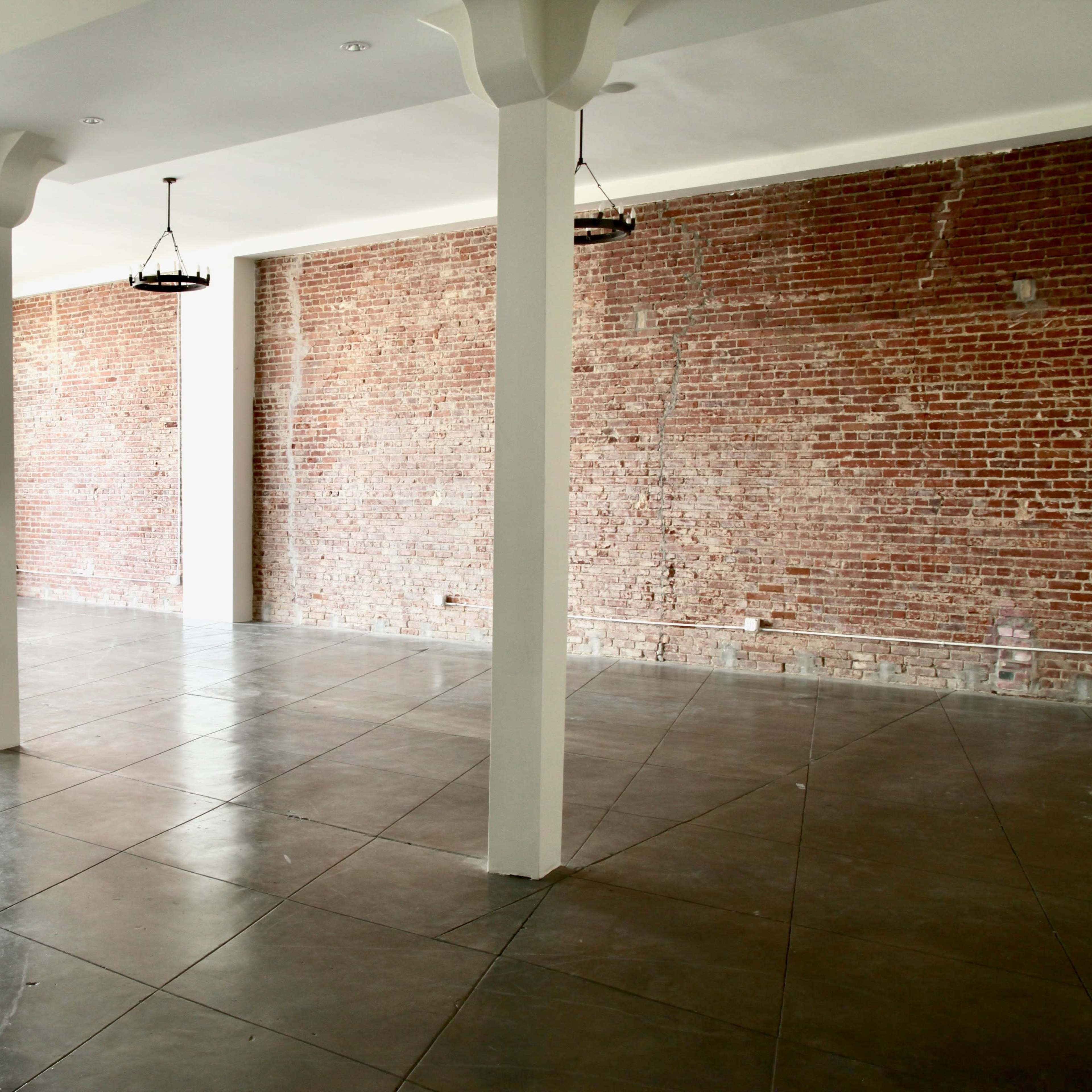 An empty room with polished concrete floors, exposed brick walls, and several pendant lights hanging from the ceiling.